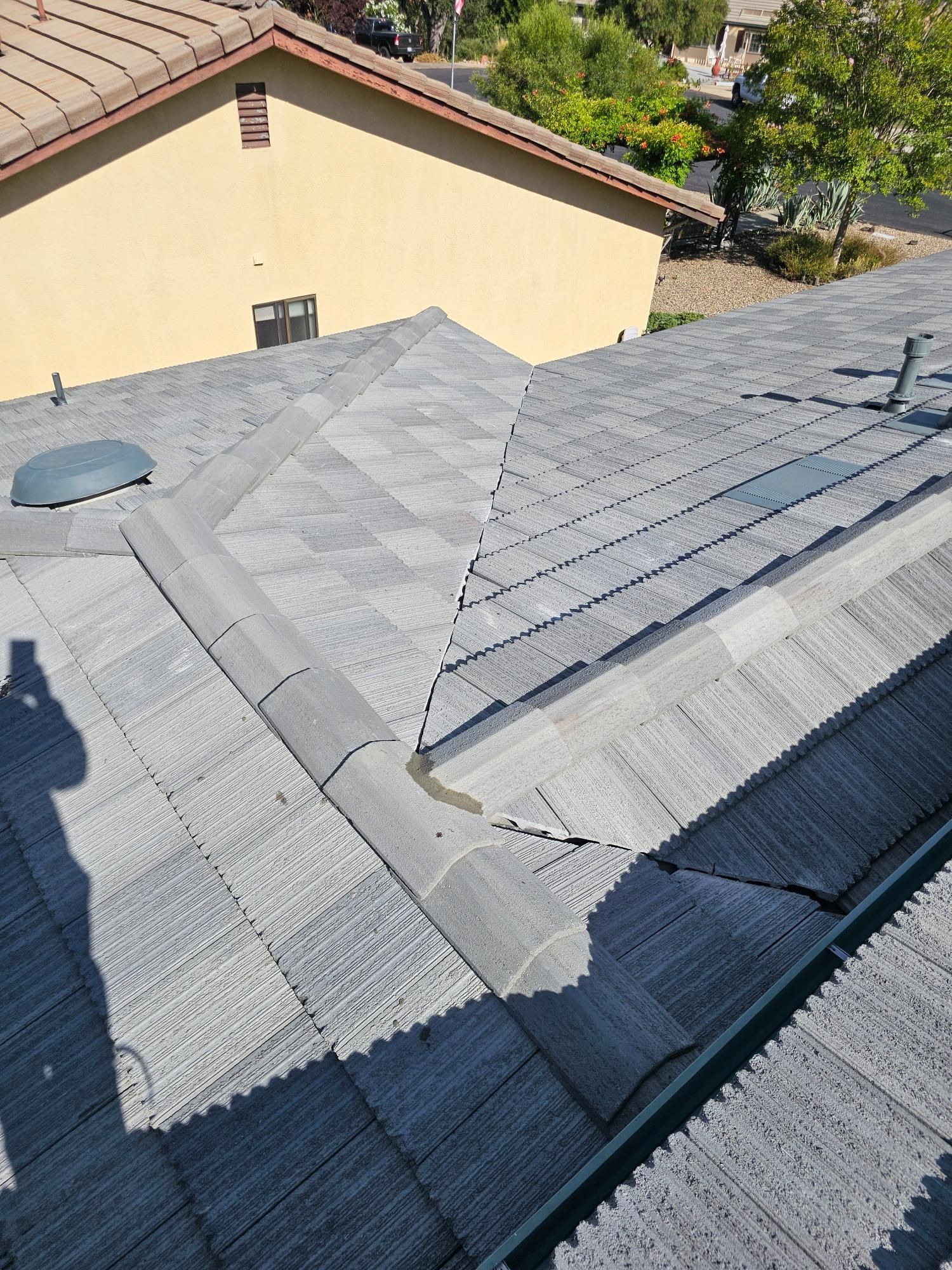 Gray shingled roof with vents and ridge lines beside a tan building on a sunny day