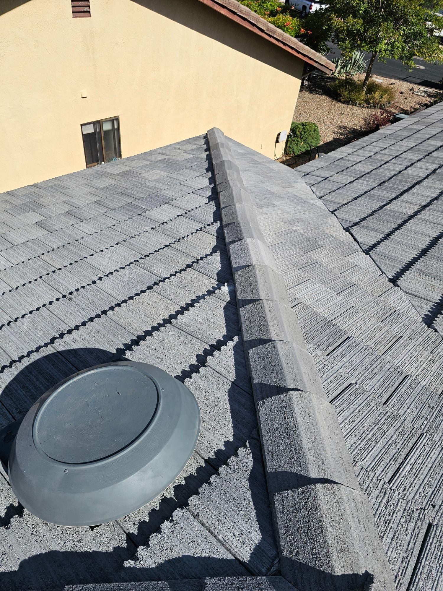 Gray shingle roof with a ridge vent and round roof vent beside a tan house wall