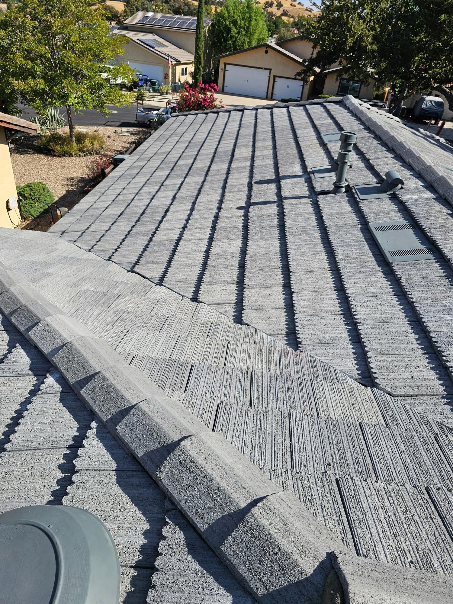 Close-up of a gray textured roof with raised seams, viewed from above in bright sunlight.