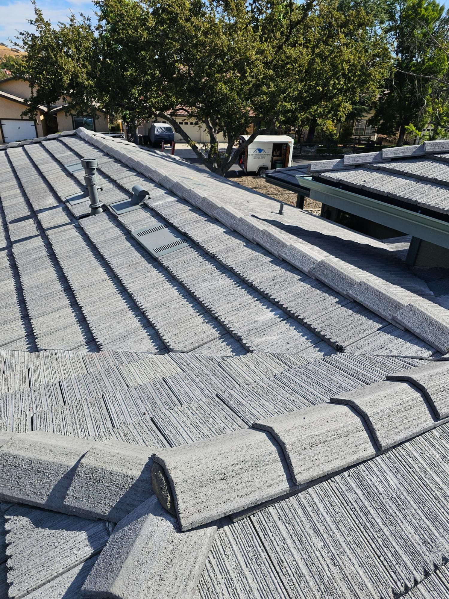 Gray shingled roof with a roof vent and gutters, seen from above on a sunny day