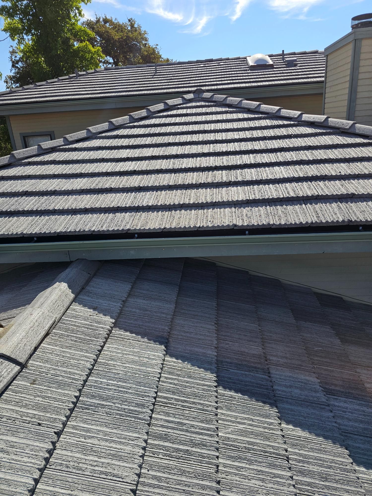 Slate-gray shingled roof with a valley and dormer under a blue sky, viewed from above.