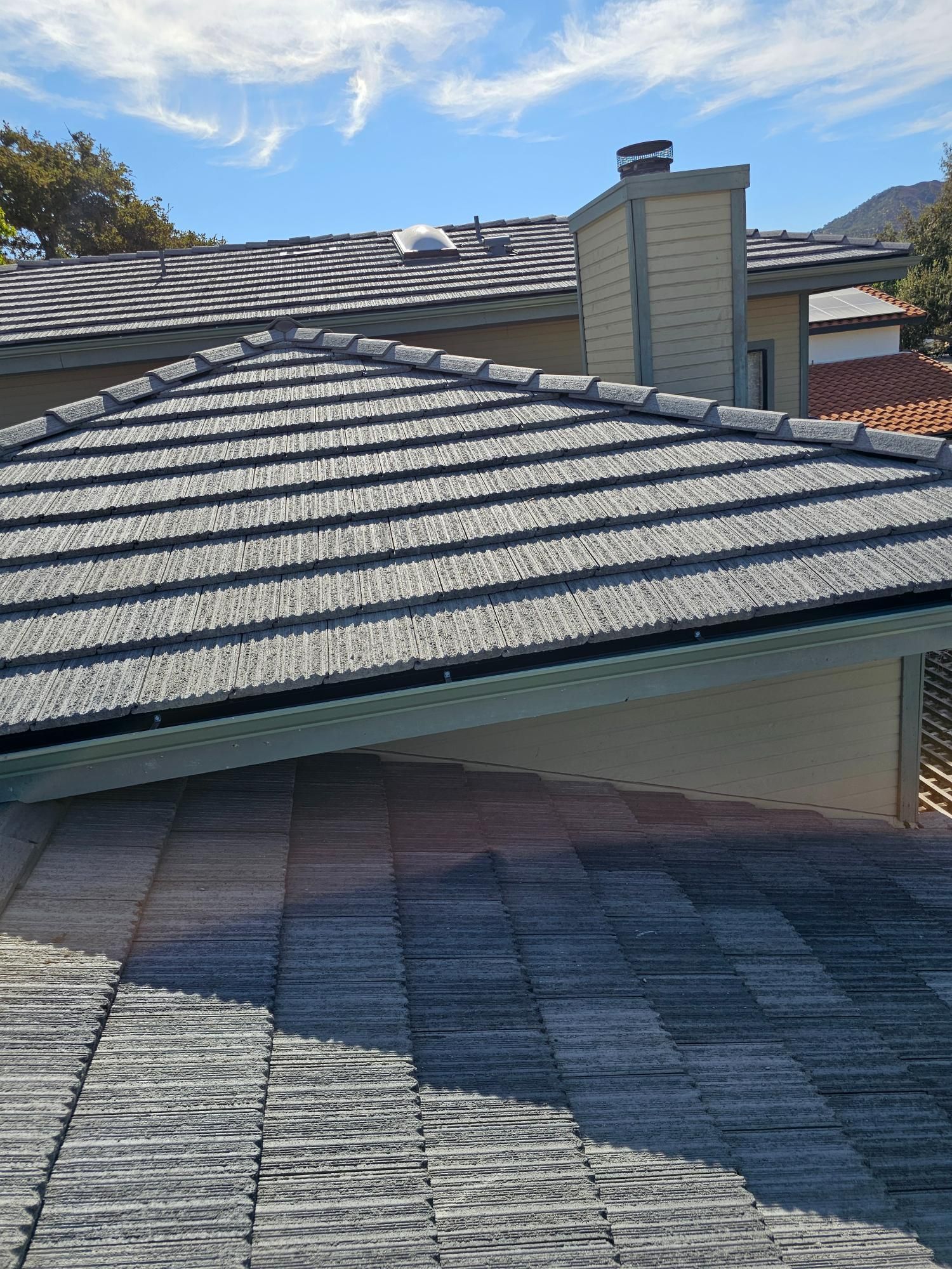 Close-up of gray shingle roof with chimney against blue sky and mountains