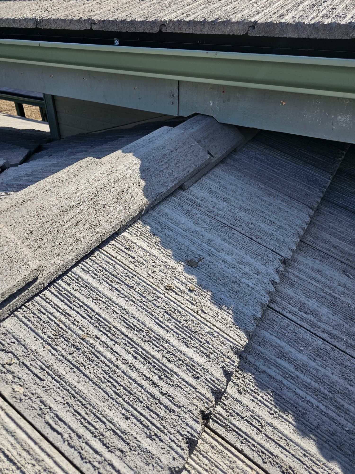 Close-up of gray roof shingles under a metal roof edge with visible damage and wear