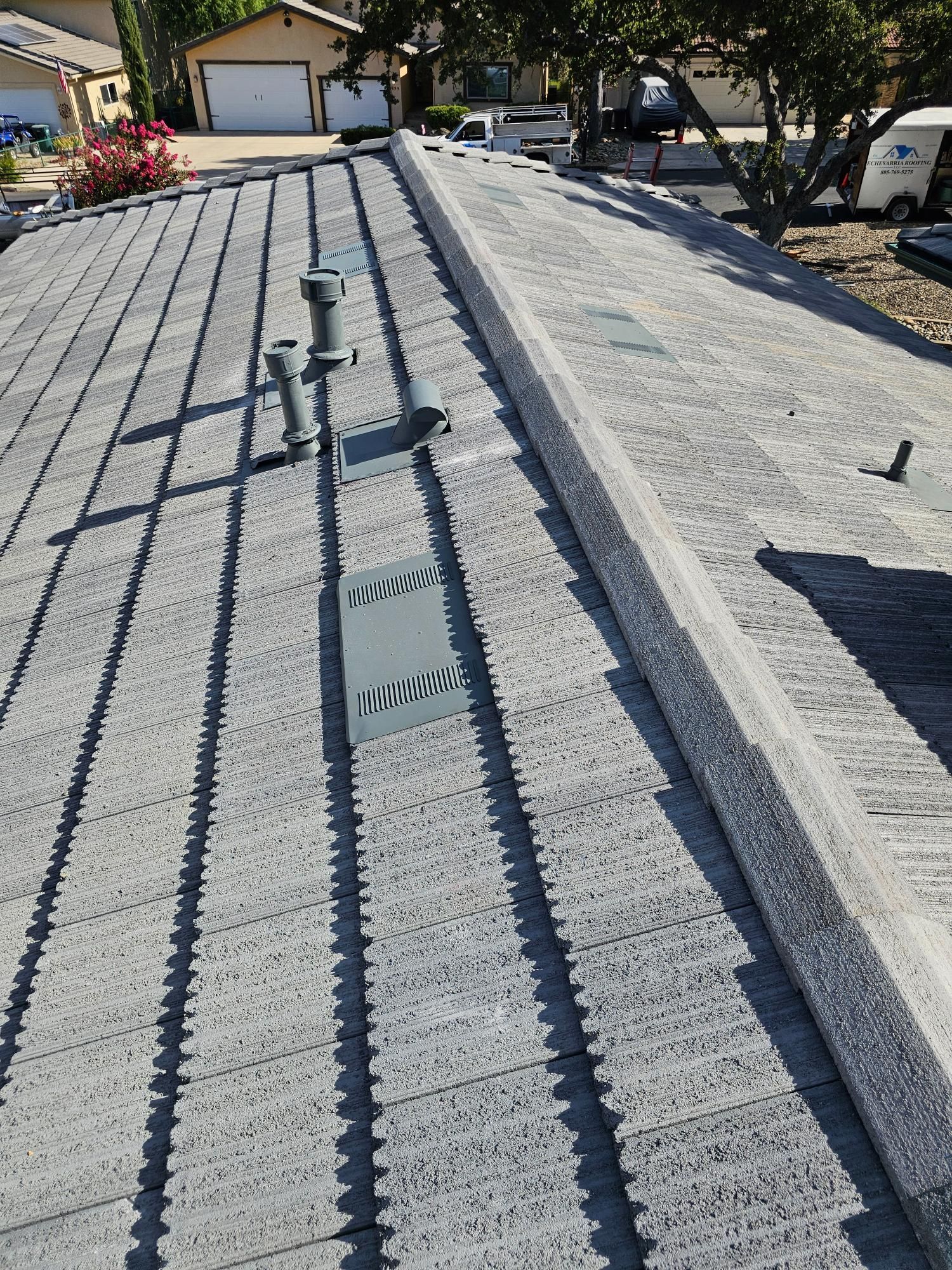 Gravel rooftop with metal vents and raised edges, viewed toward a garage and trees in bright sunlight
