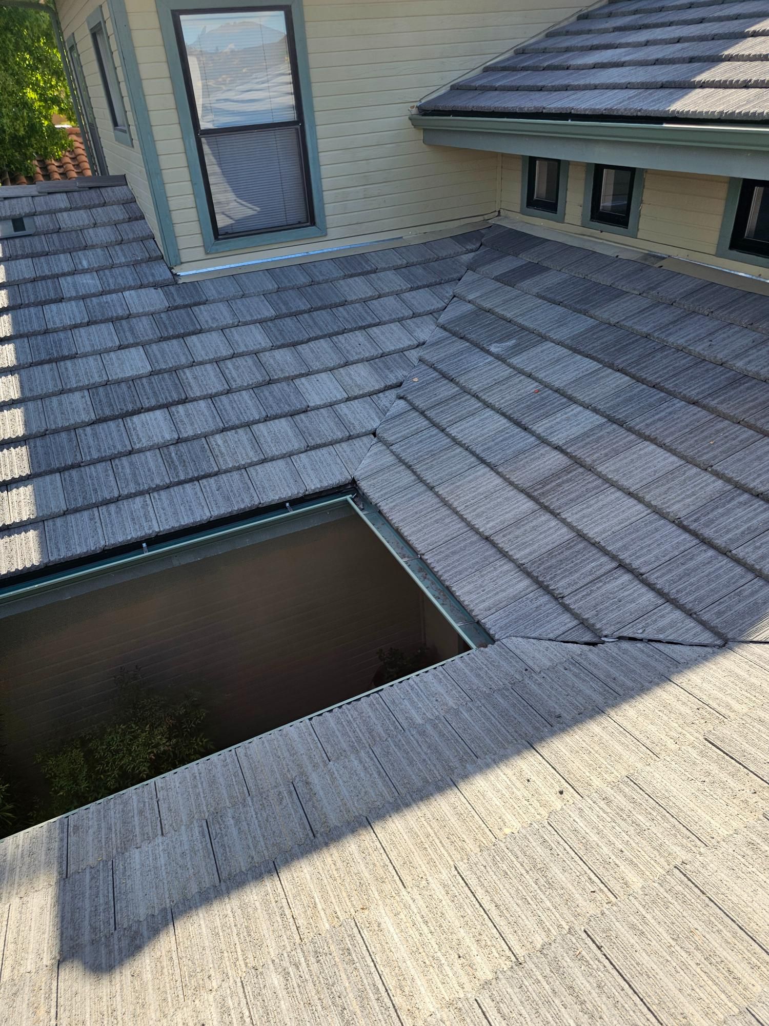 Rooftop with gray shingles, a skylight opening, and a door leading inside.