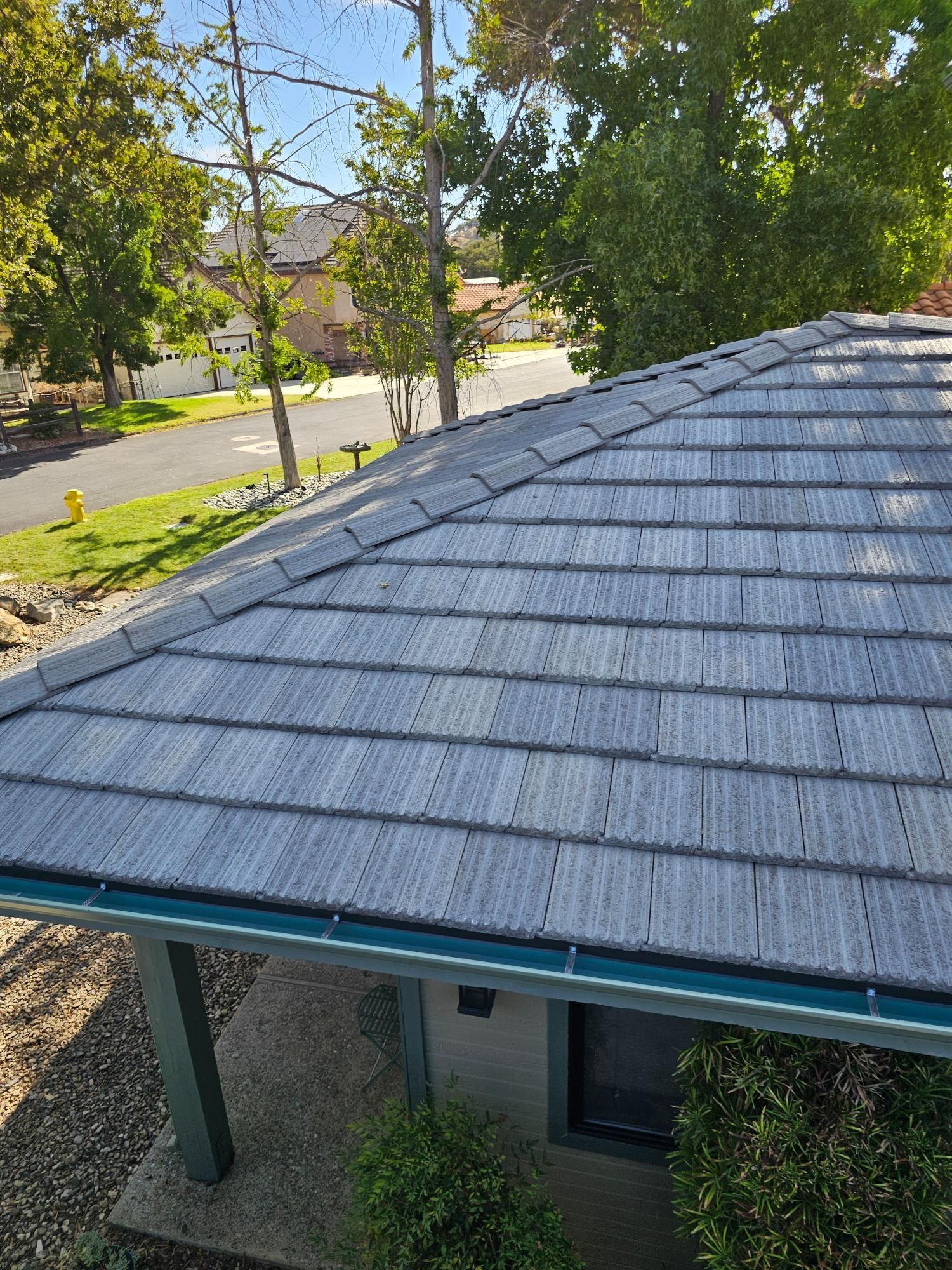 Gray shingled roof viewed from above, with trees and a suburban street in the background