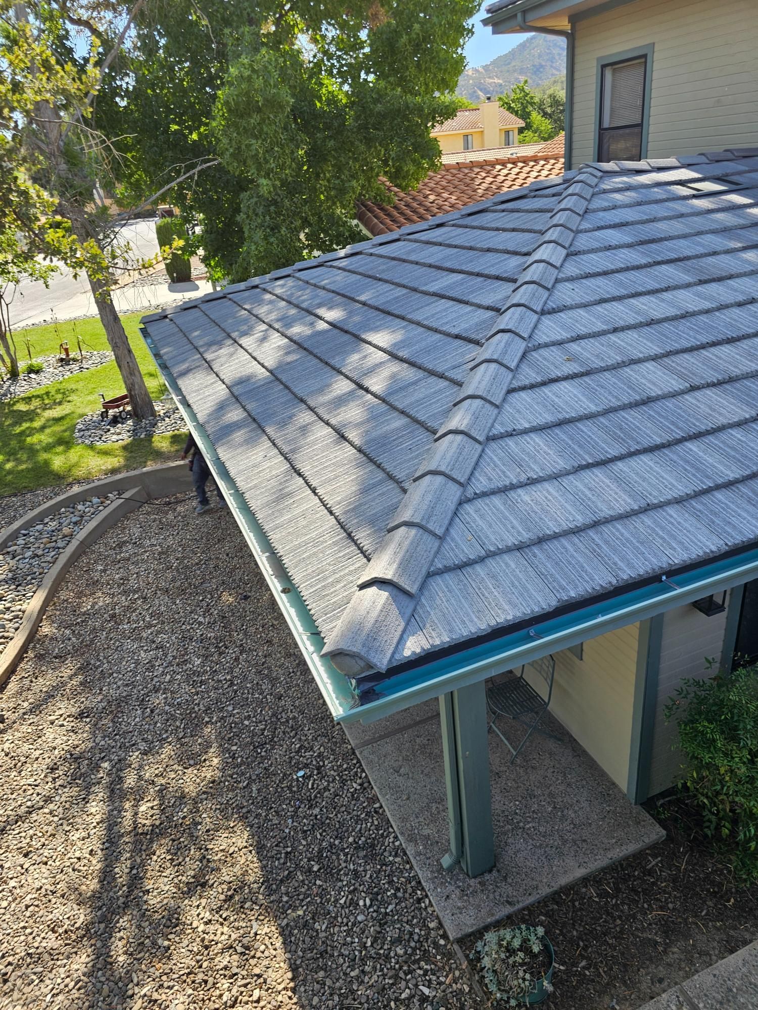 Gravel roof with gray shingles and a turquoise trim on a small house, viewed from above.