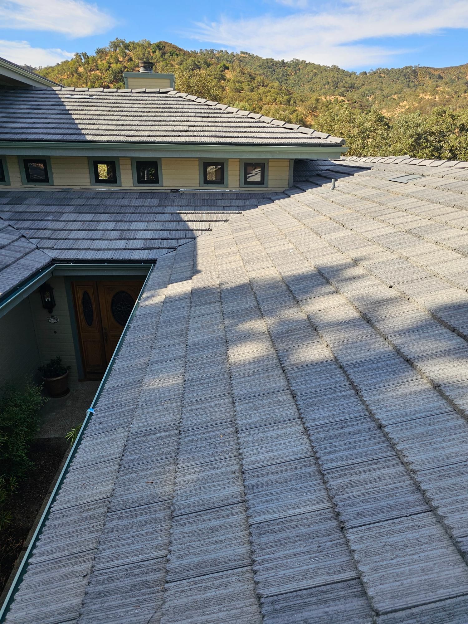 Slate roof on a modern house with skylights, backed by trees and hills under sunlight