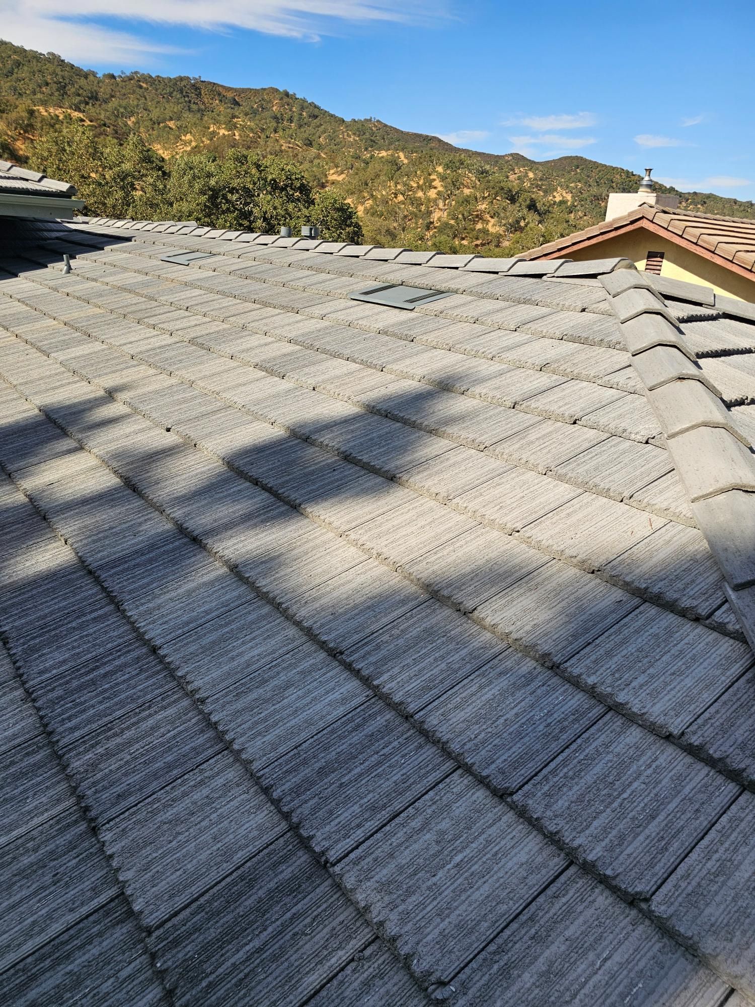Gray shingle roof with long shadows, backed by sunlit hills and a red-roofed house corner