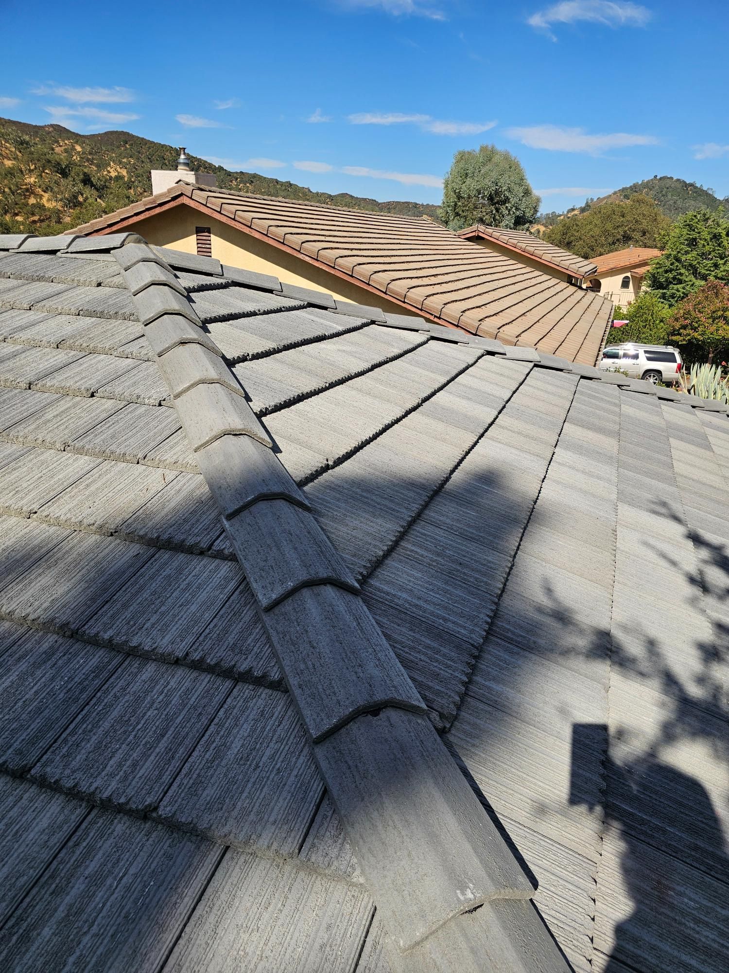 Rooftop view of gray shingle and red tile roofs with hills and blue sky in the background