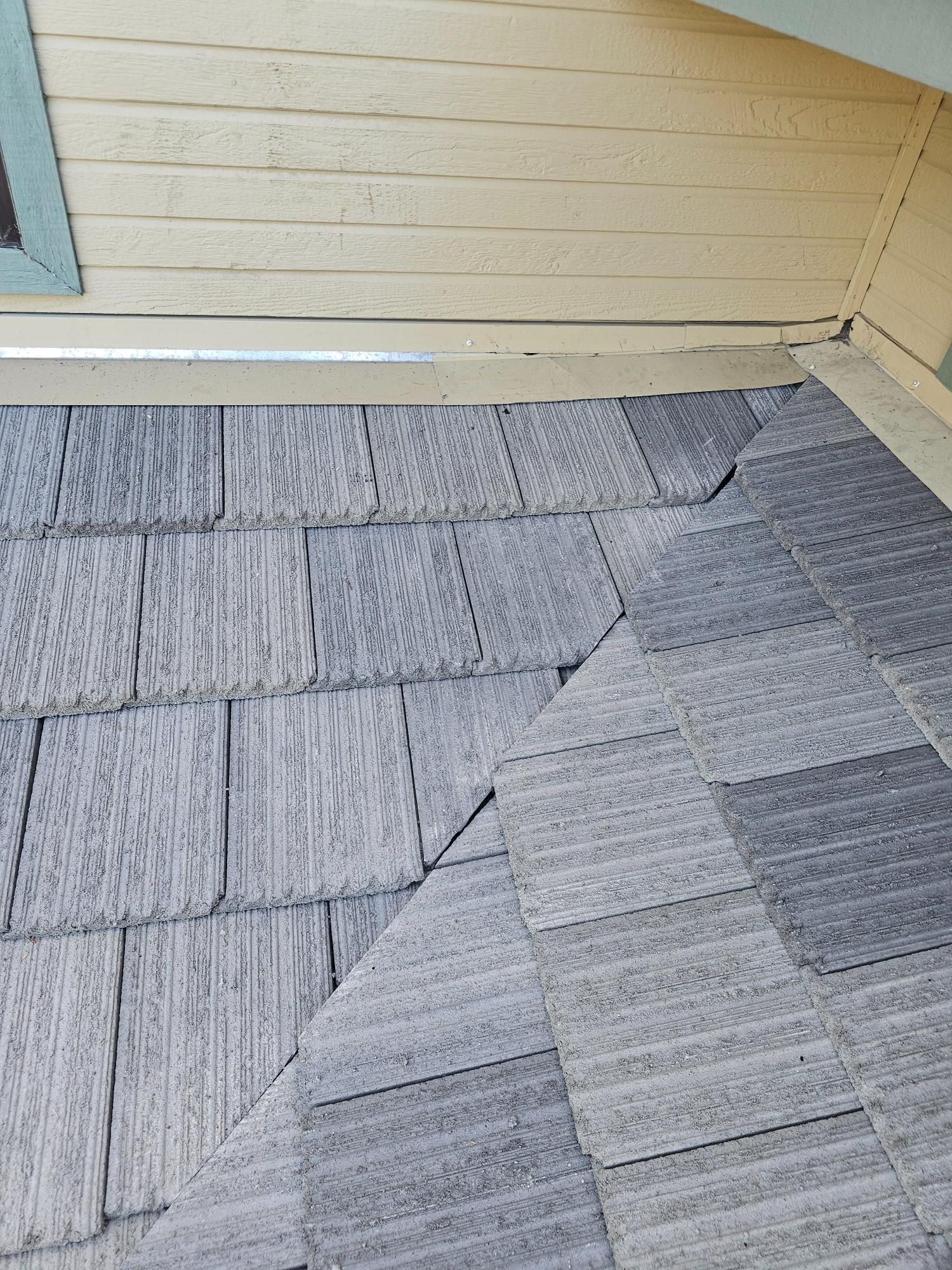 Gray shingle roof meeting a beige wall under a window corner