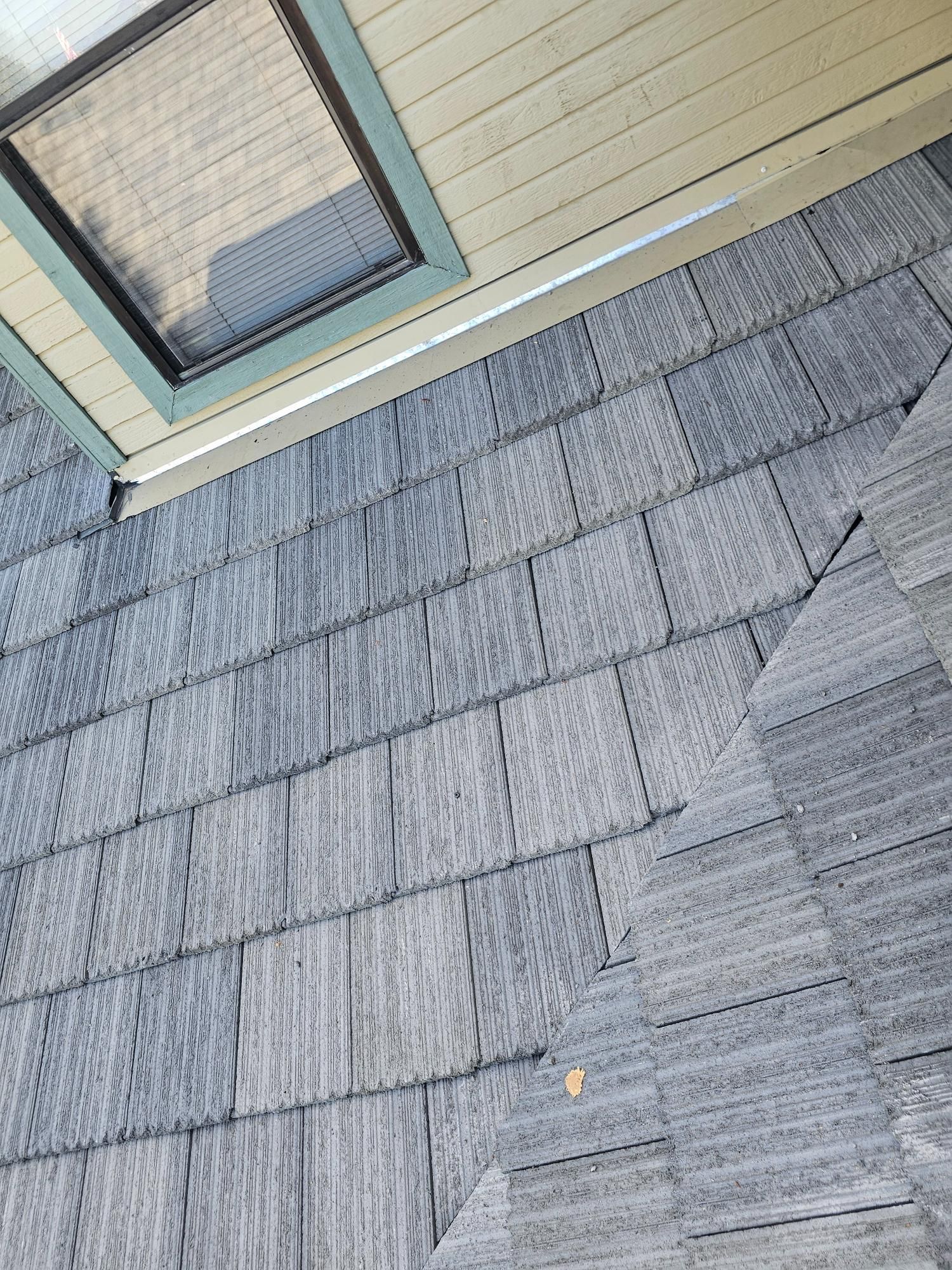 Gray shingle roof beside beige siding and a window, viewed at an angle