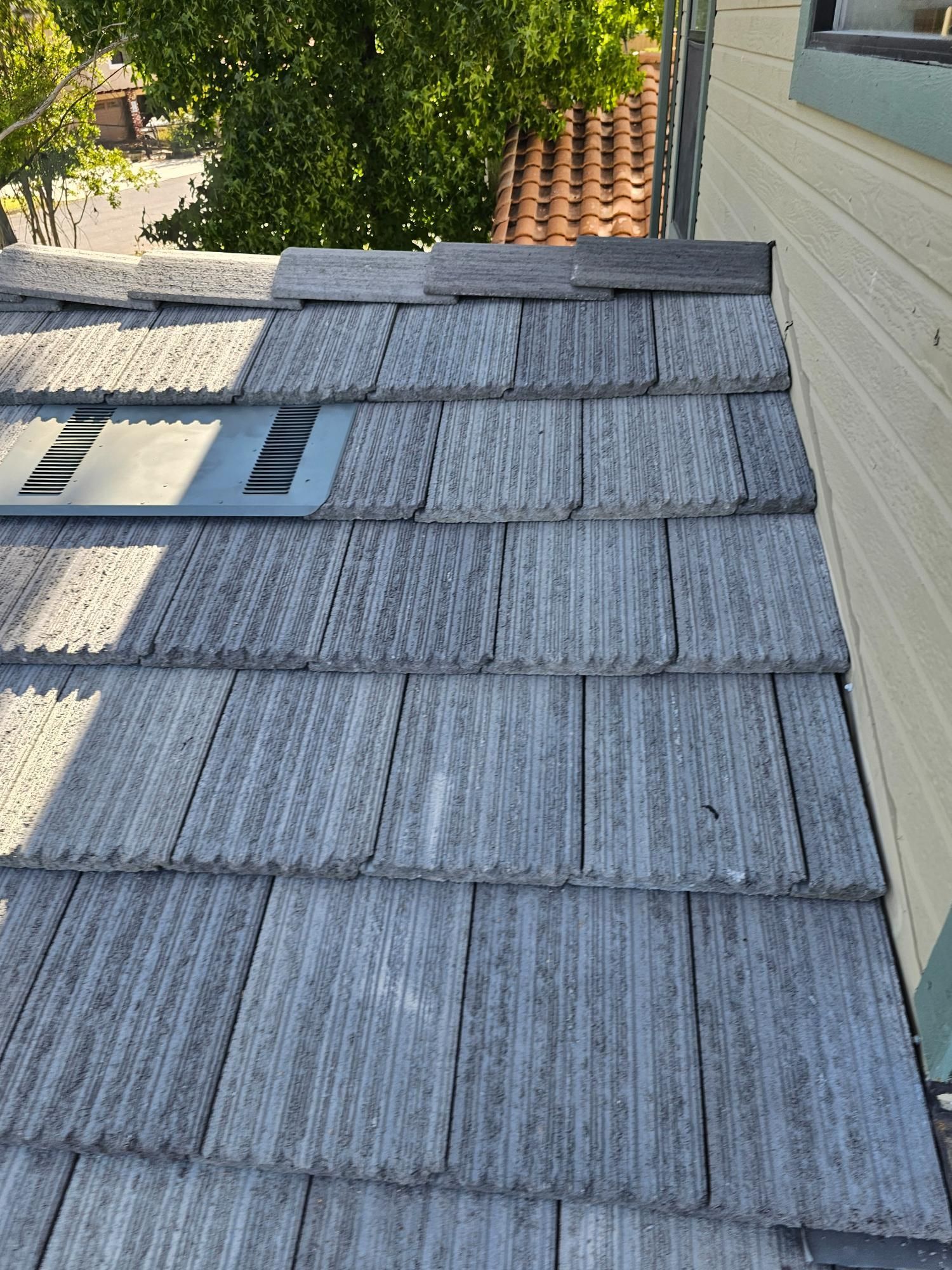 Roof shingles beside a house wall, with a skylight and trees in the background.