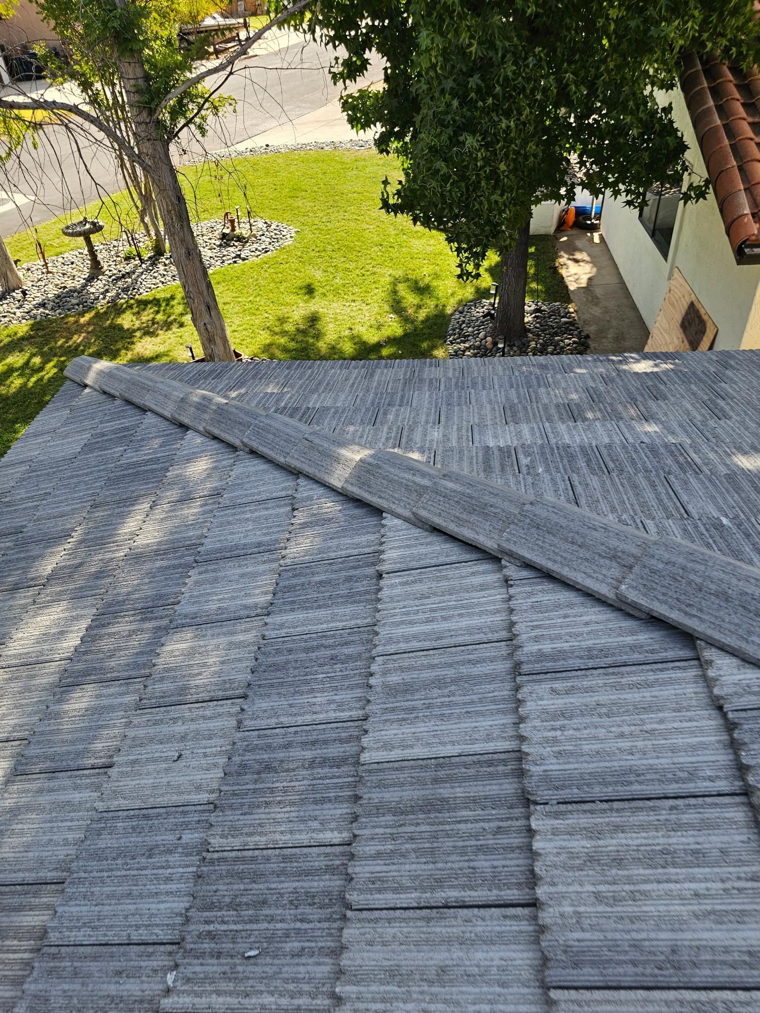 Steep gray shingle roof overlooking a green yard with trees and a walkway below