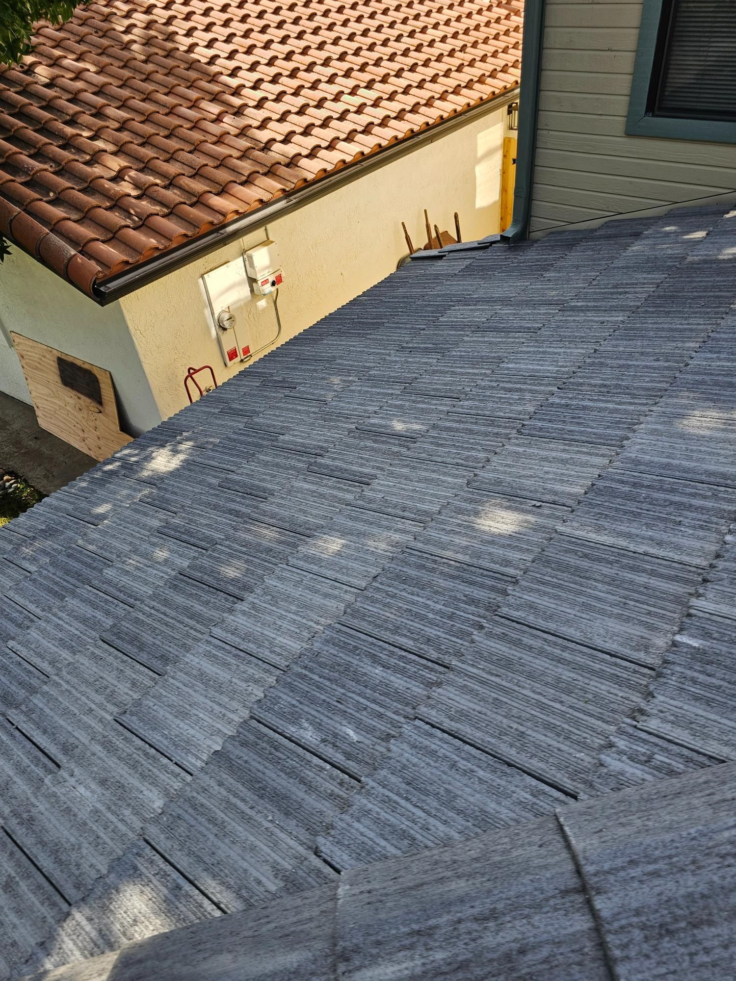 Rooftop with blue-gray shingles beside a tan house and a red-tiled roof.