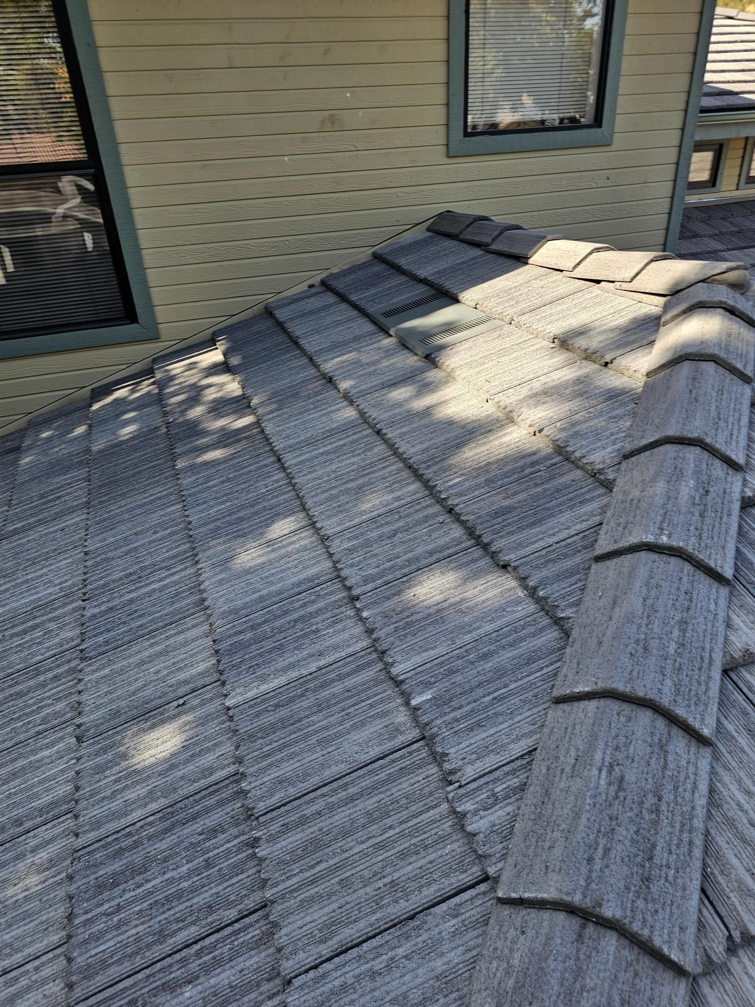 Roof covered with a weathered gray tarp beside tan house siding and windows