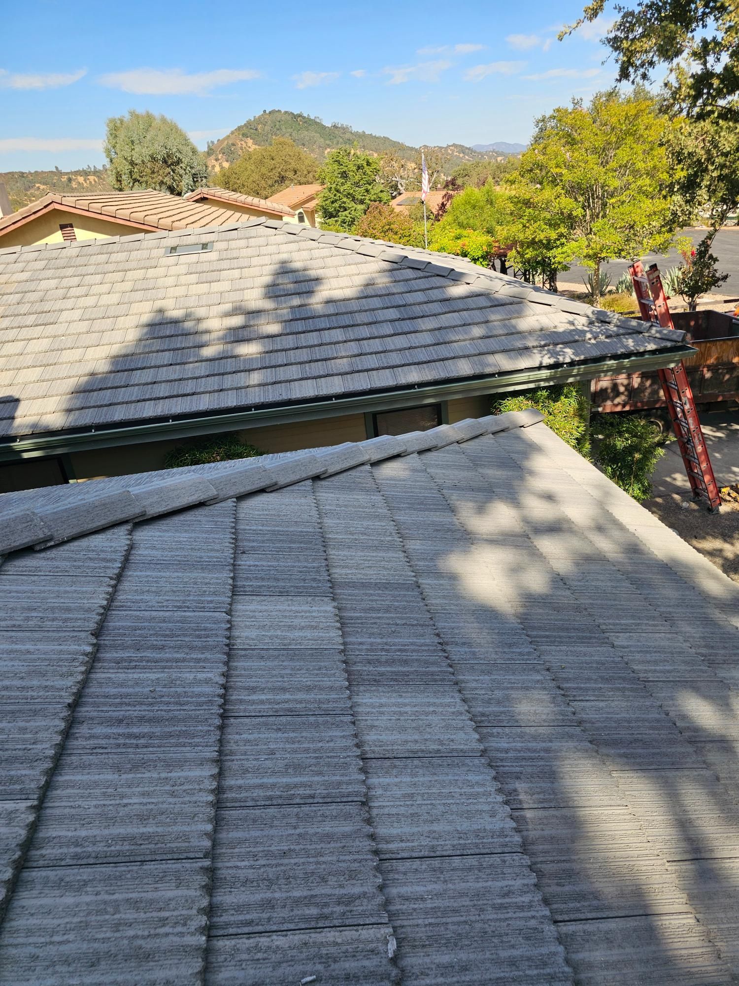 Rooftop shingles with a scenic view of trees and hills under a clear blue sky.