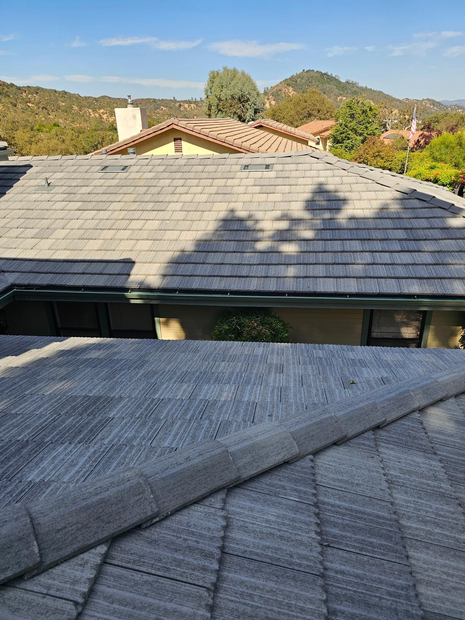 Rooftops with gray shingles in a sunny suburban neighborhood, with hills and trees in the background
