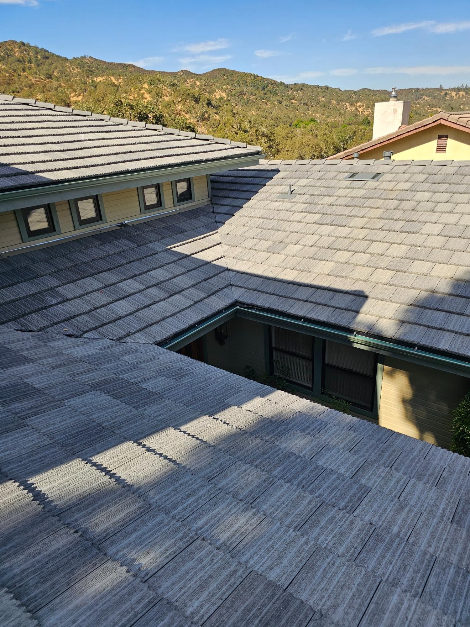 Rooftops with gray shingles in bright sunlight, with hills in the background.