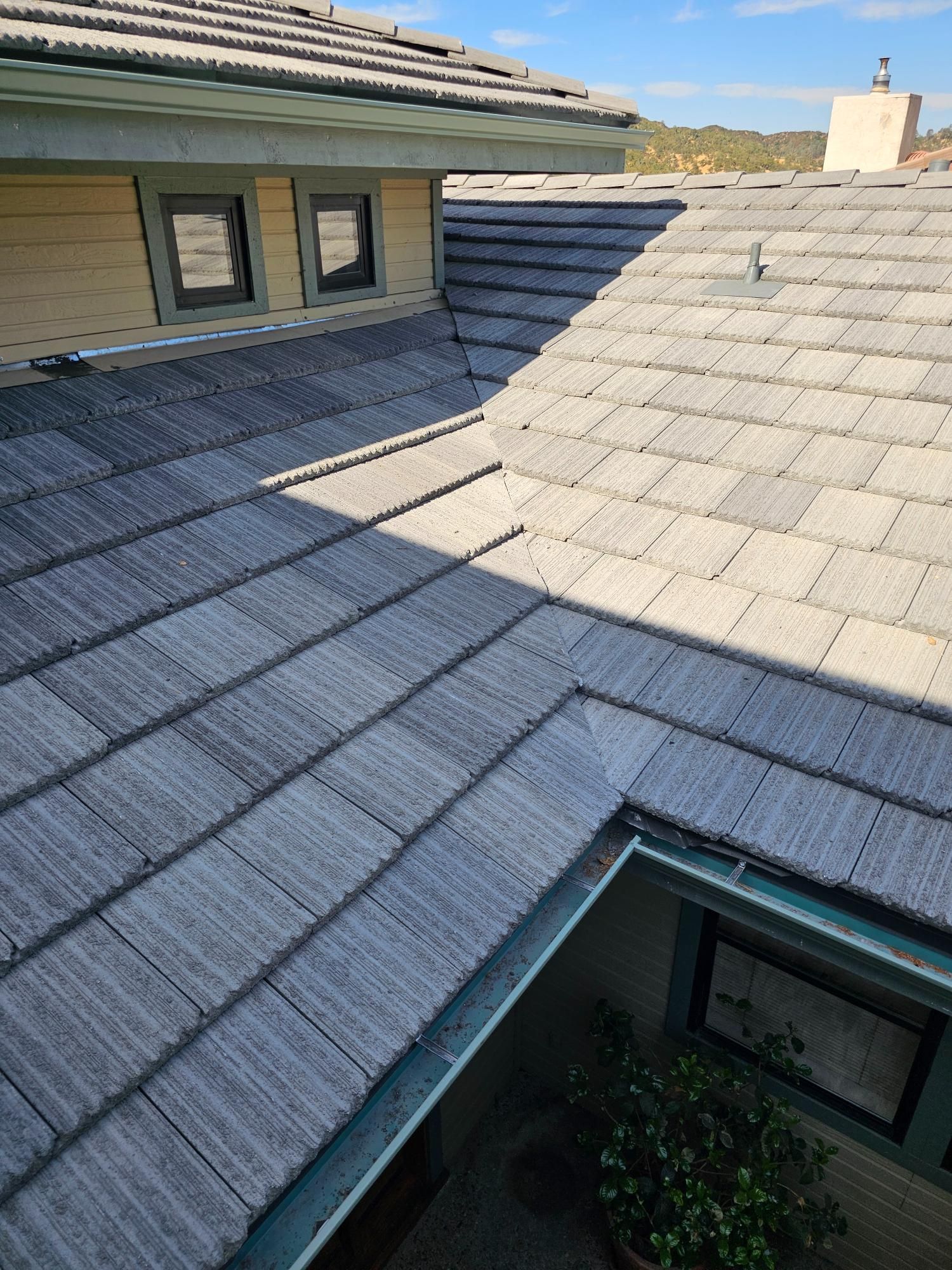 Sunlit gray shingle roof with skylight and a house wall in the background