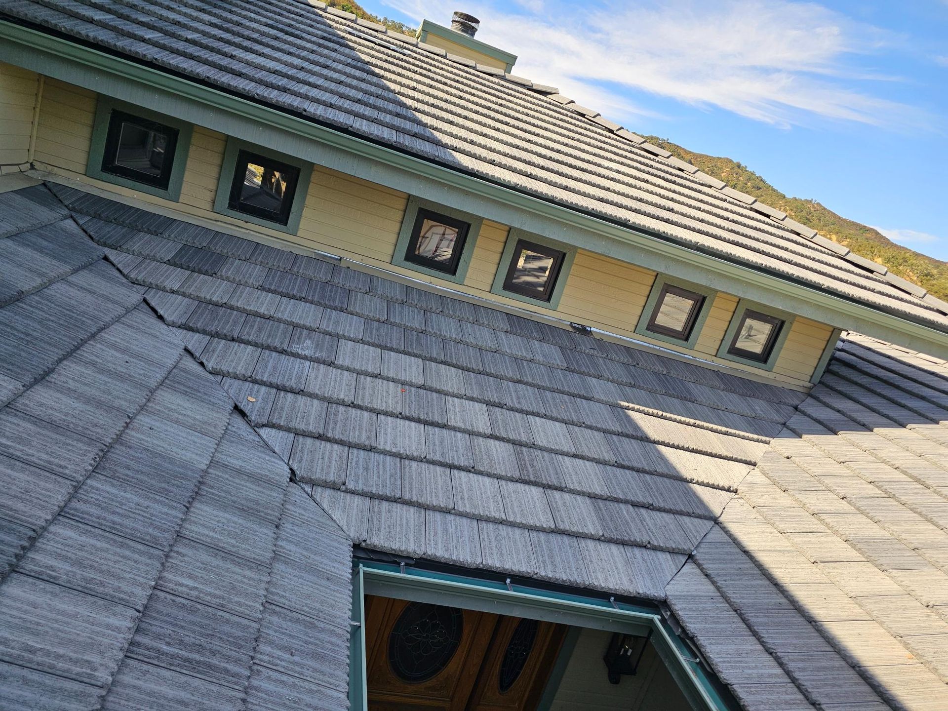 Tilted view of a gray shingled roof with dormer windows and a skylight opening