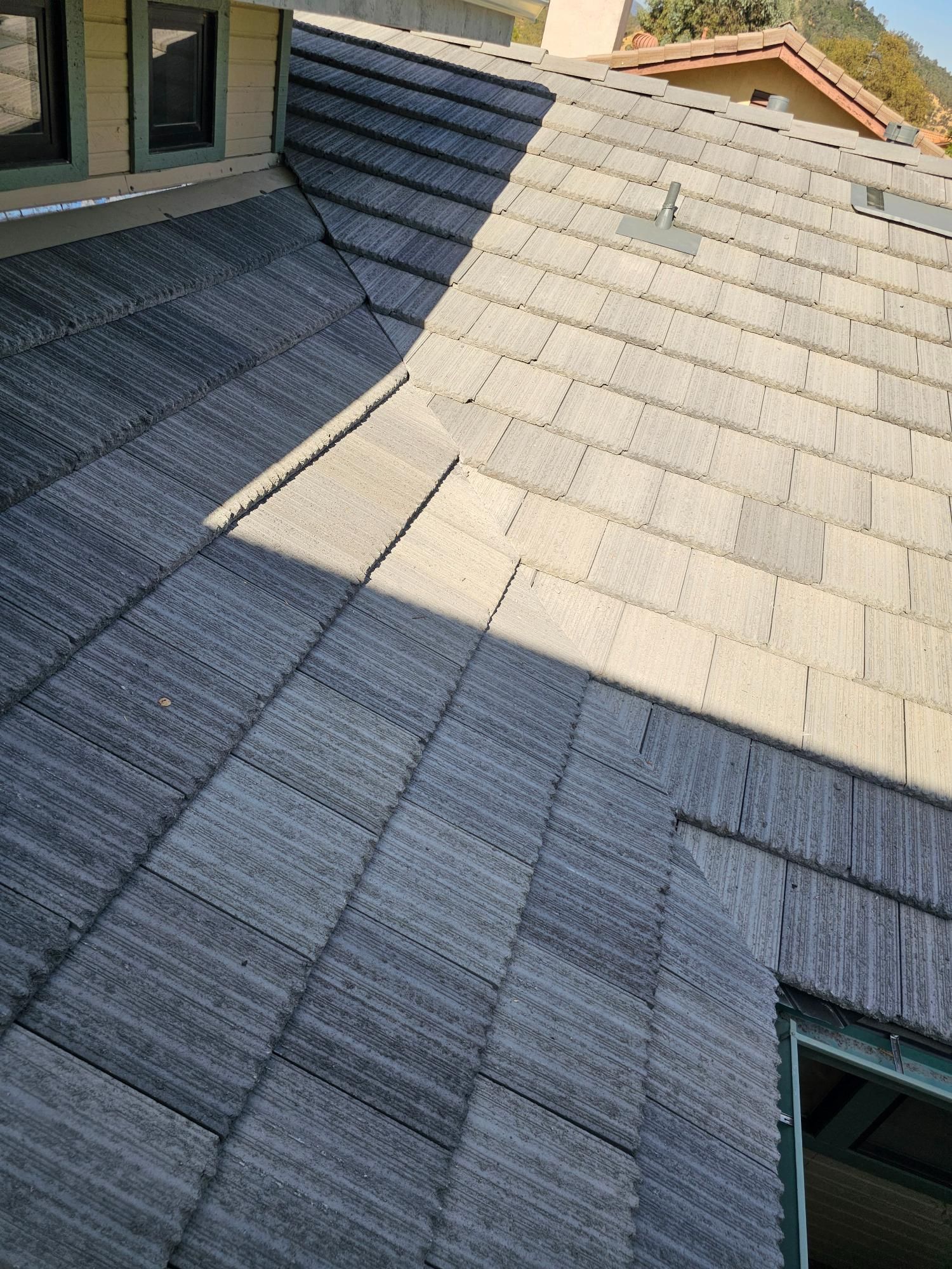 Sunlit gray shingle roof with two intersecting slopes and a skylight opening