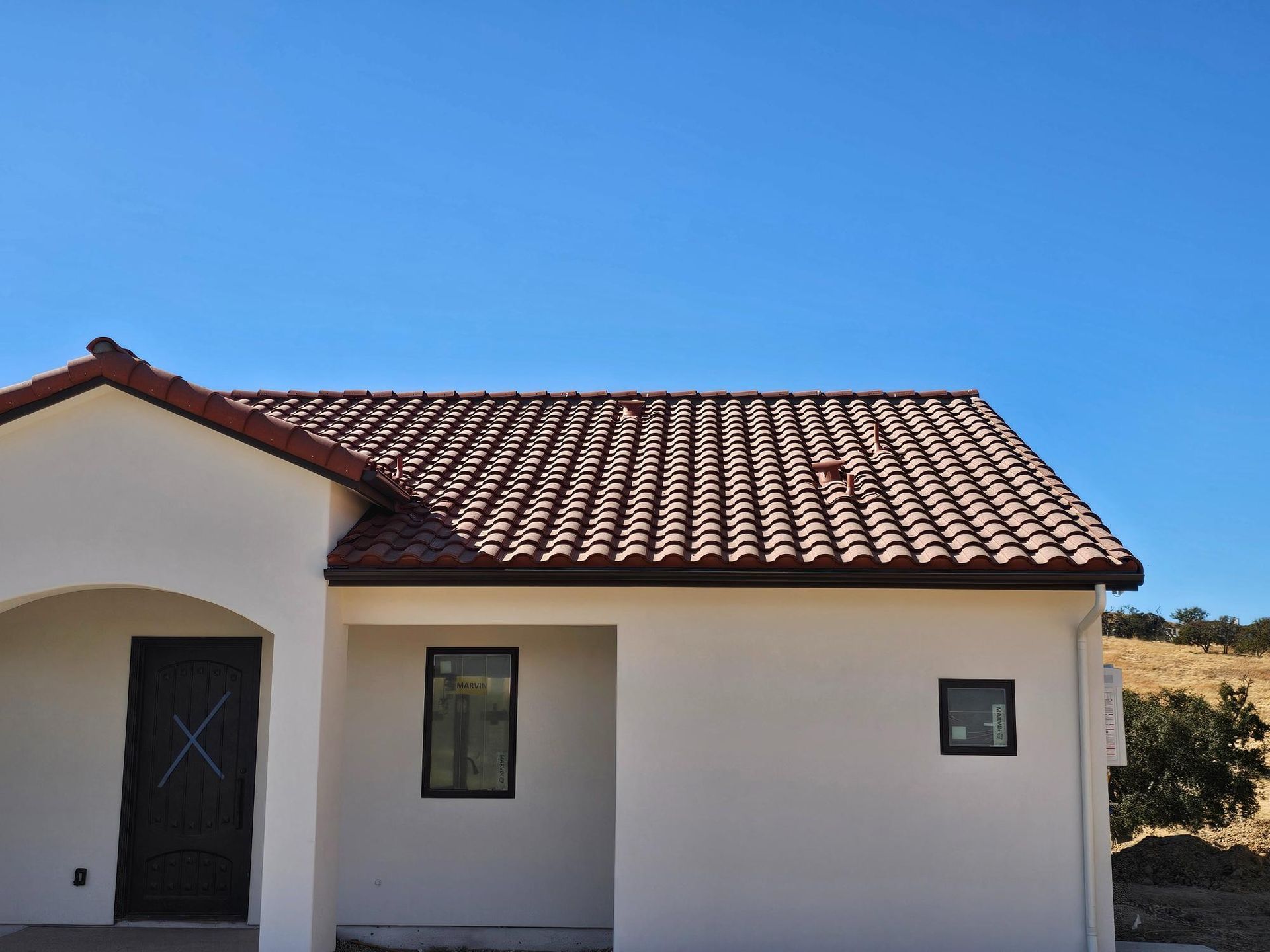 Small white stucco house with a red tile roof under a clear blue sky