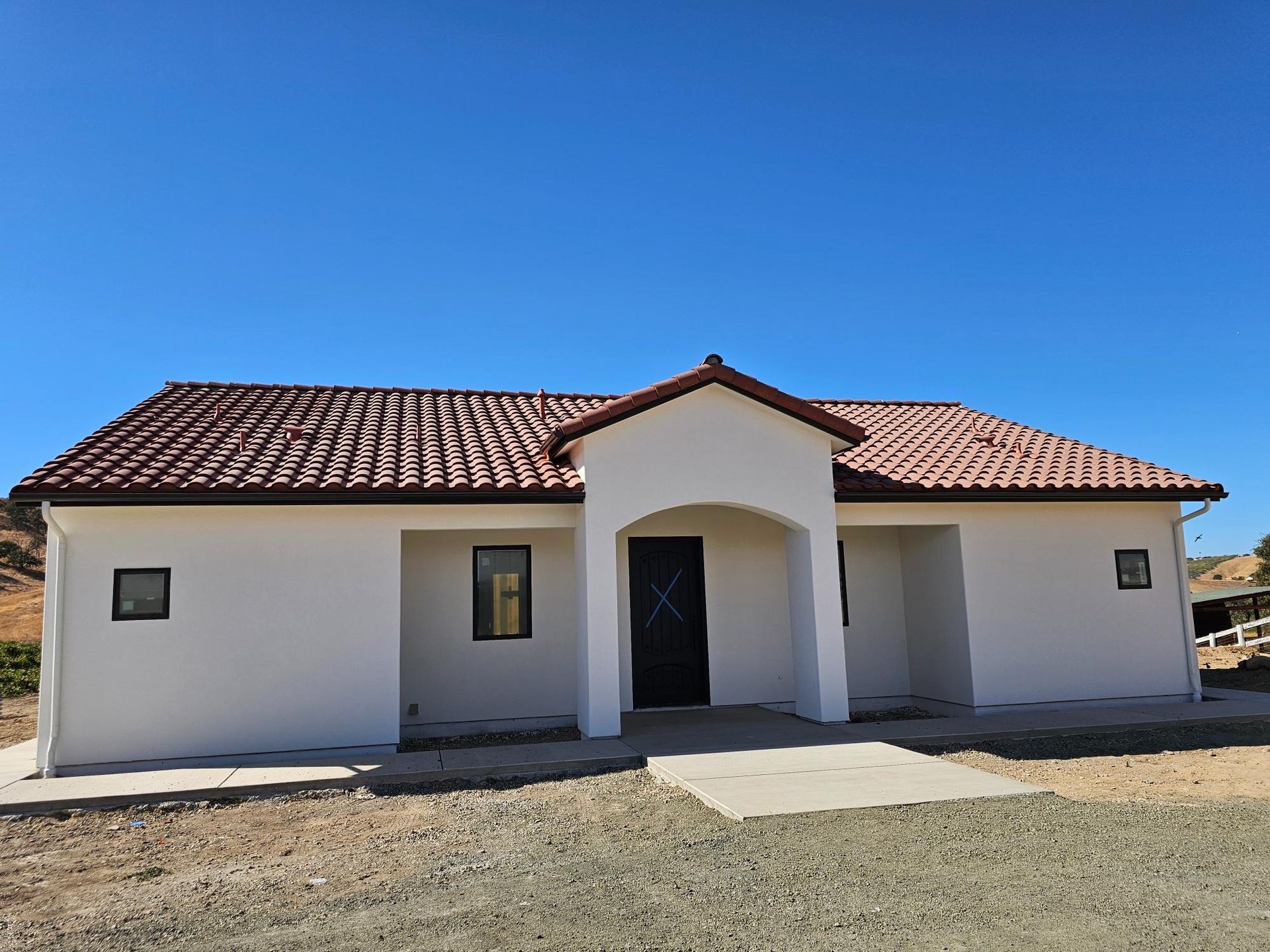 Single-story white house with red tile roof and front porch under a clear blue sky