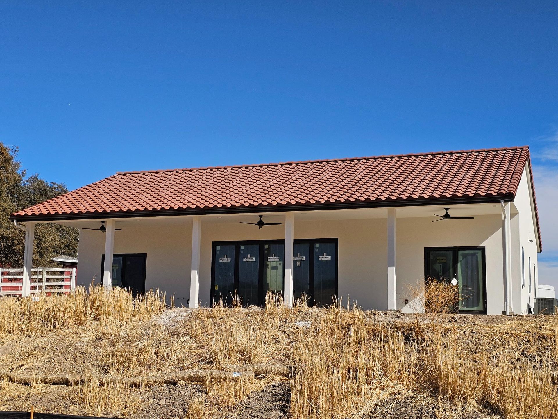 Small beige stucco house with a red tile roof on a dry hillside under a blue sky