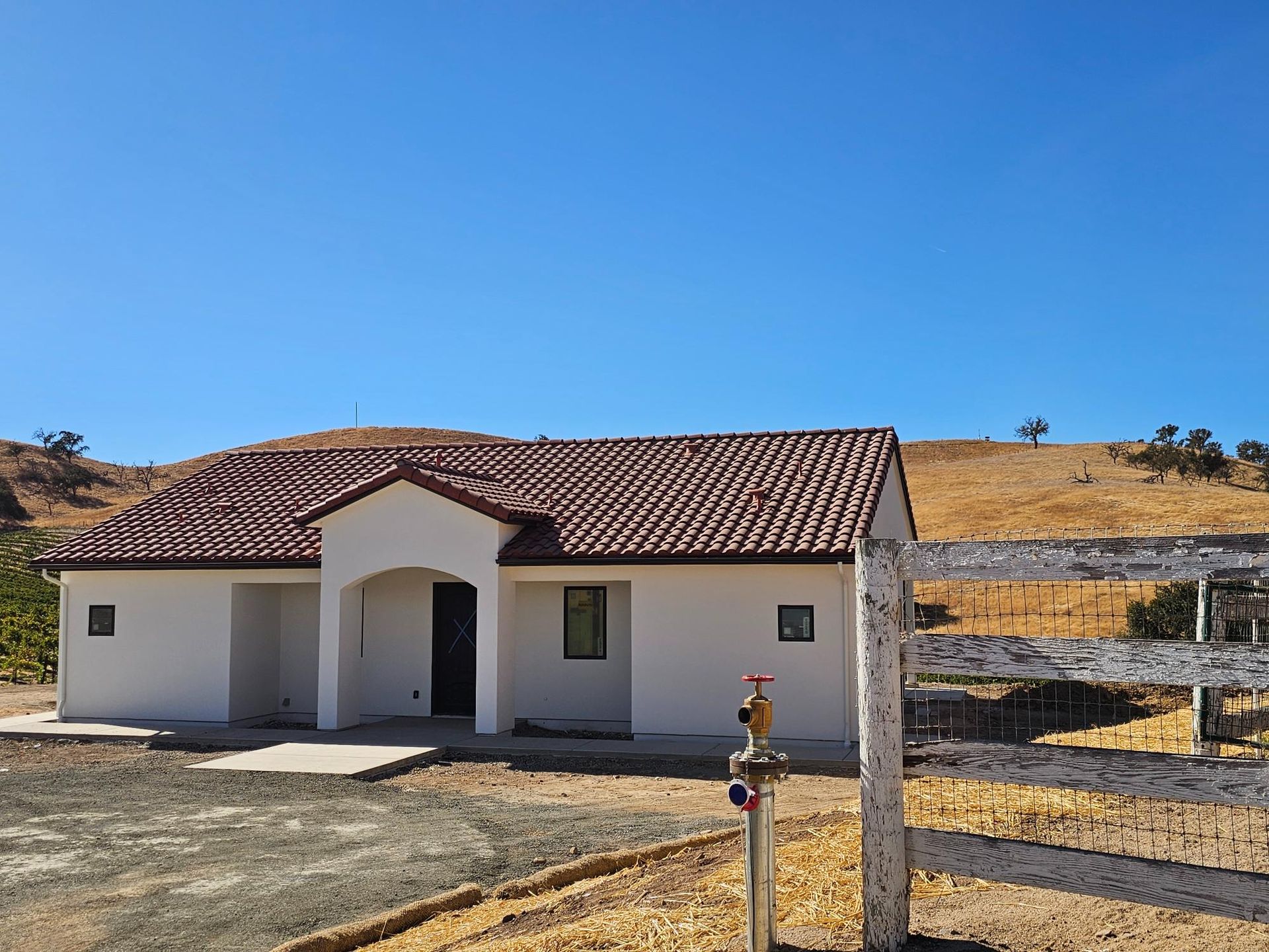 Small white house with a red tile roof in a dry rural landscape under a clear blue sky