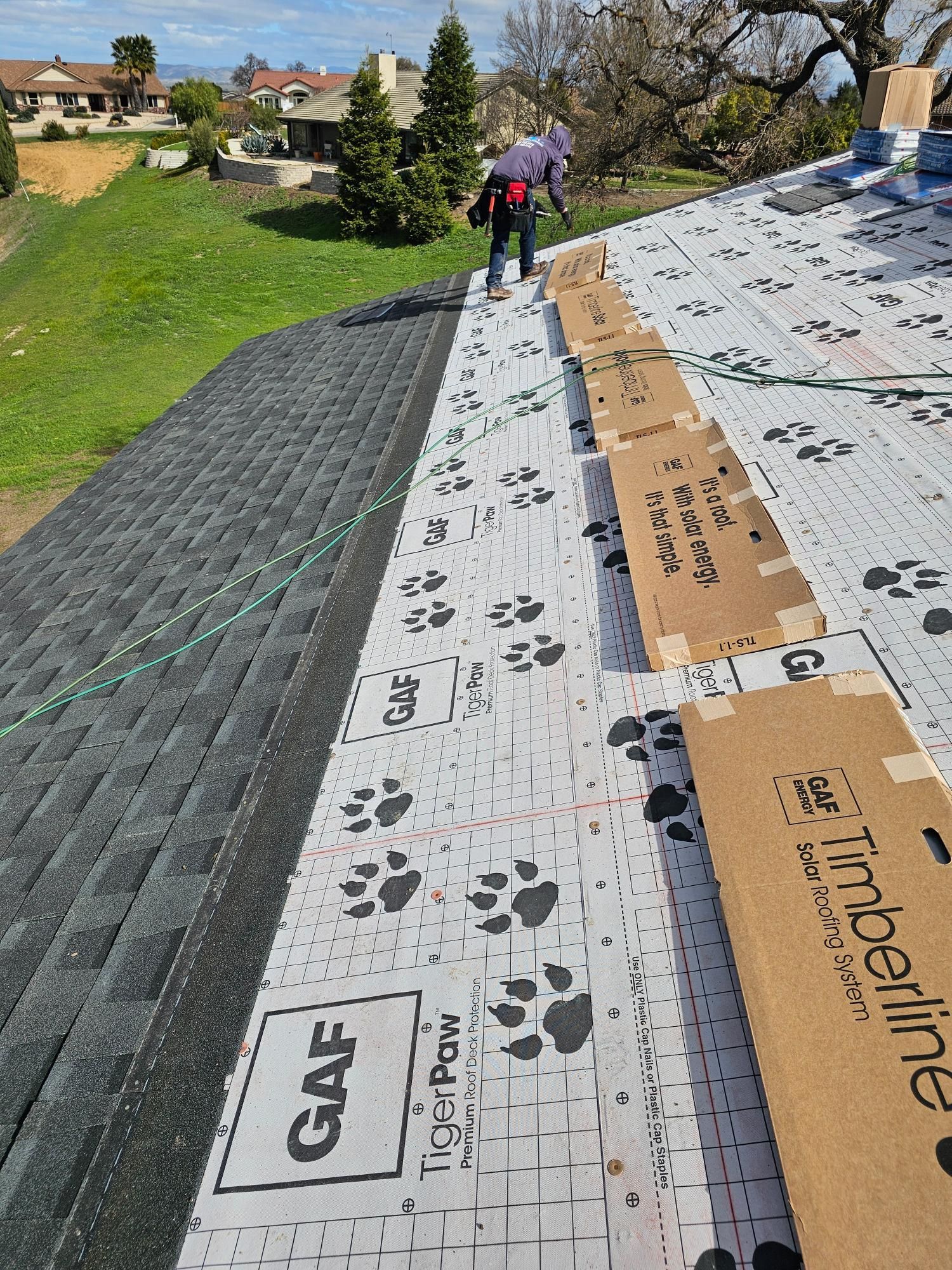Worker on a sloped roof installing black underlayment and white roofing membrane.