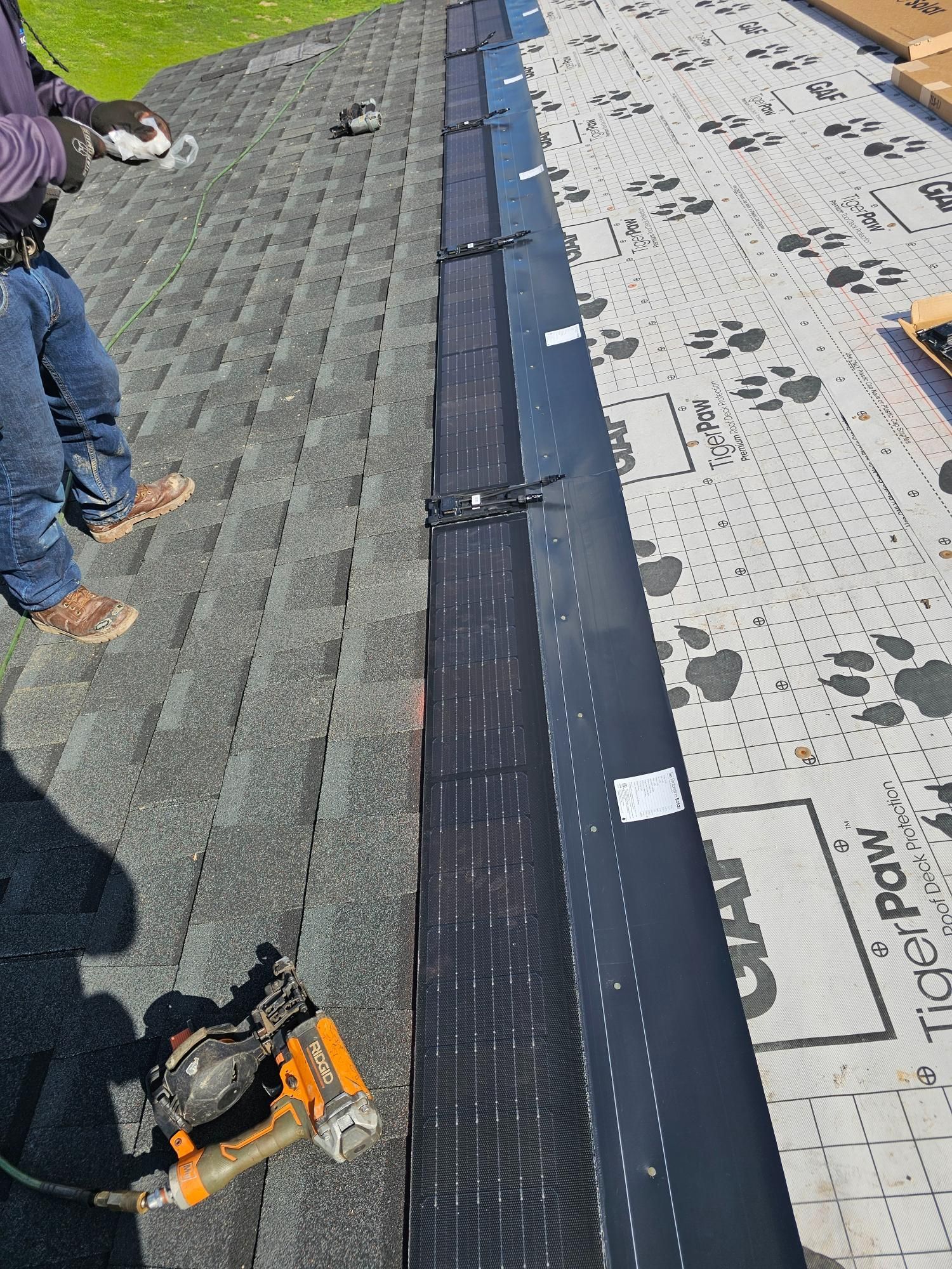 Roof with workers installing a black roof vent strip between gray shingles and underlayment.