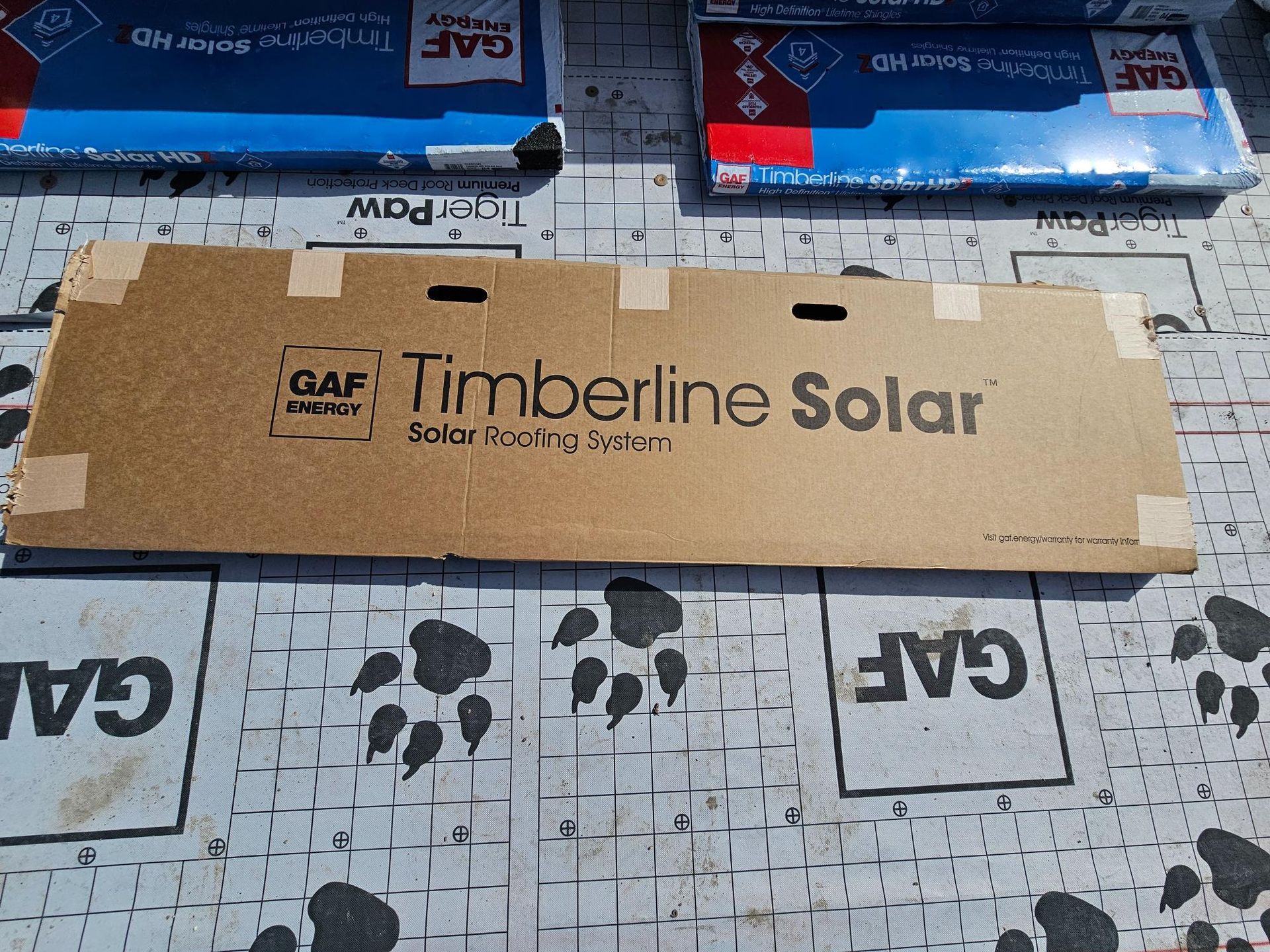 Cardboard GAF Timberline Solar box on a work surface with blue packaged items above it