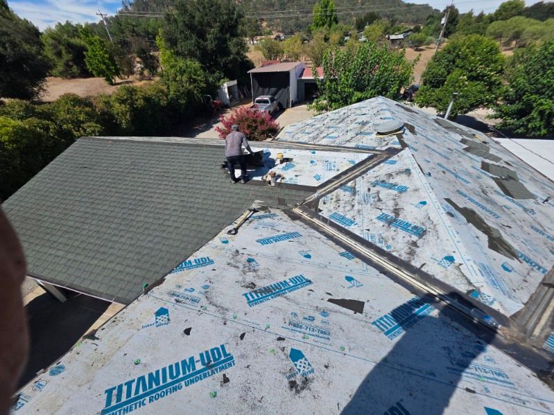 Roof under repair with gray underlayment, blue tarp, and rooftop vent in a sunny suburban neighborhood