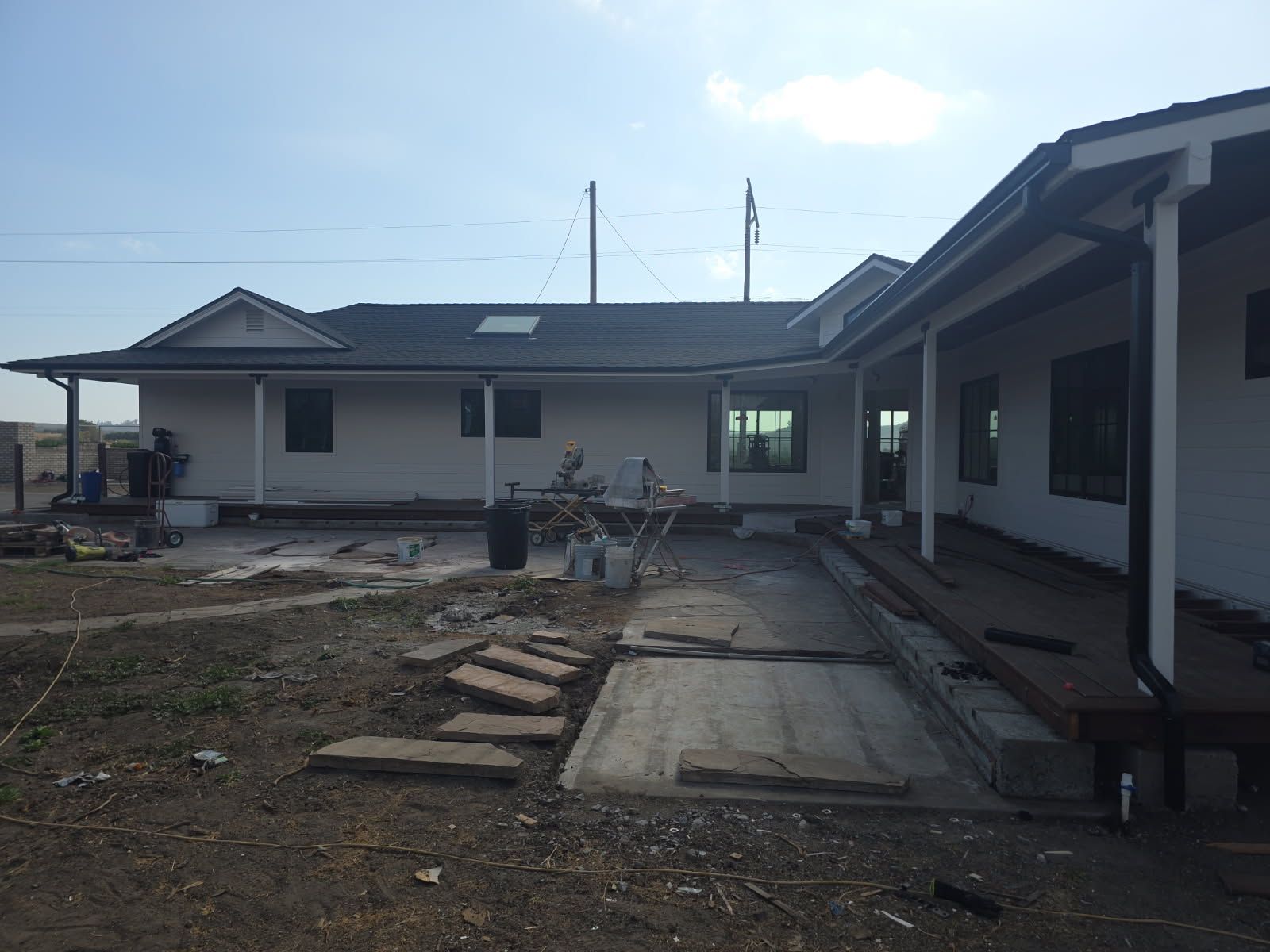 Backyard patio construction with a concrete slab, dirt path, and single-story house under a cloudy sky