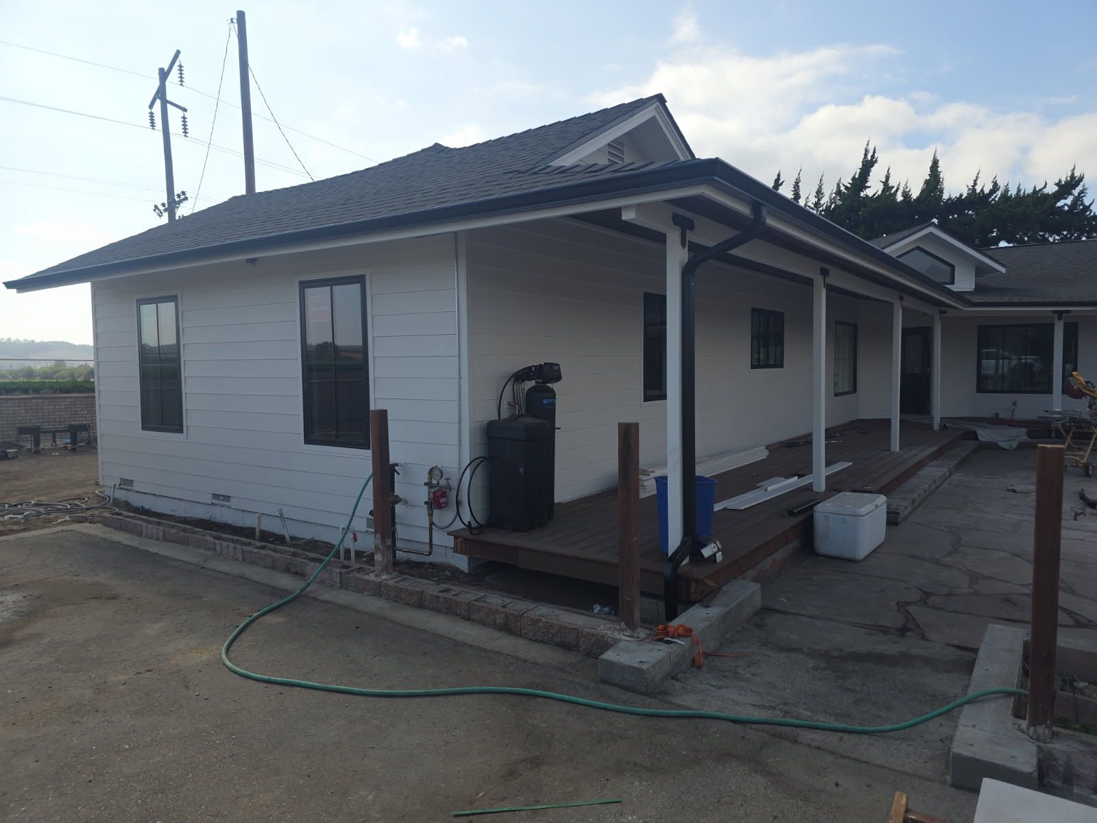 Small white house with a dark roof and porch, seen from the side with a hose in the yard