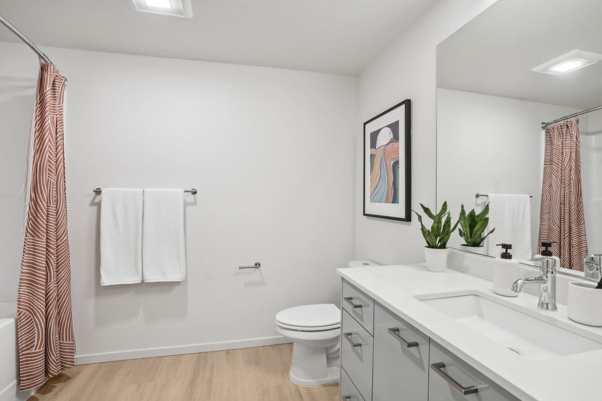 Bright modern bathroom with double vanity, toilet, large mirror, white walls, and pink shower curtain