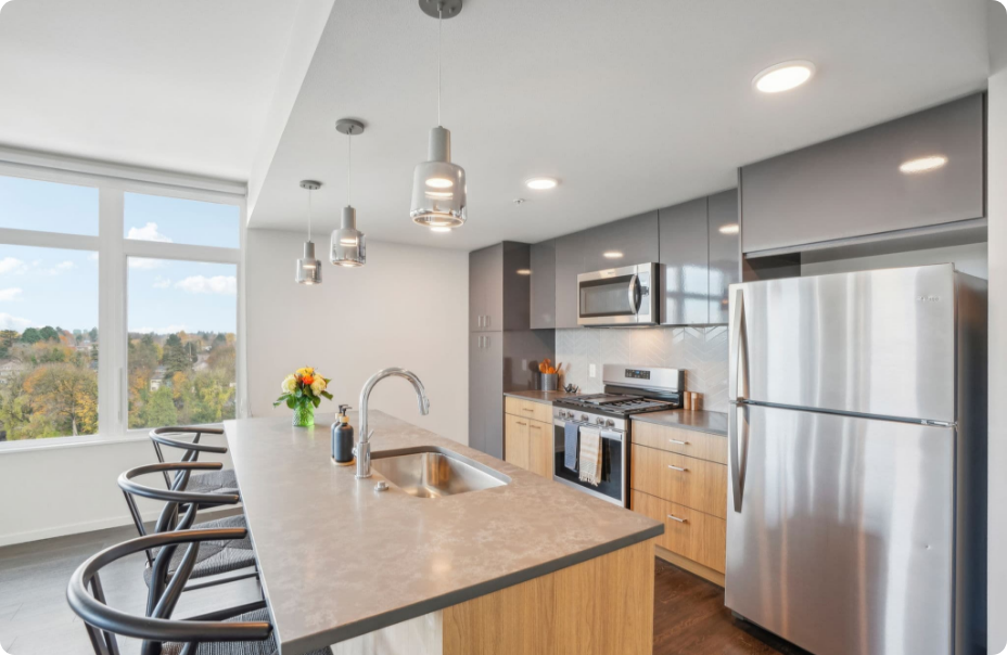 Modern kitchen with stainless steel appliances, island seating, and large windows overlooking greenery.