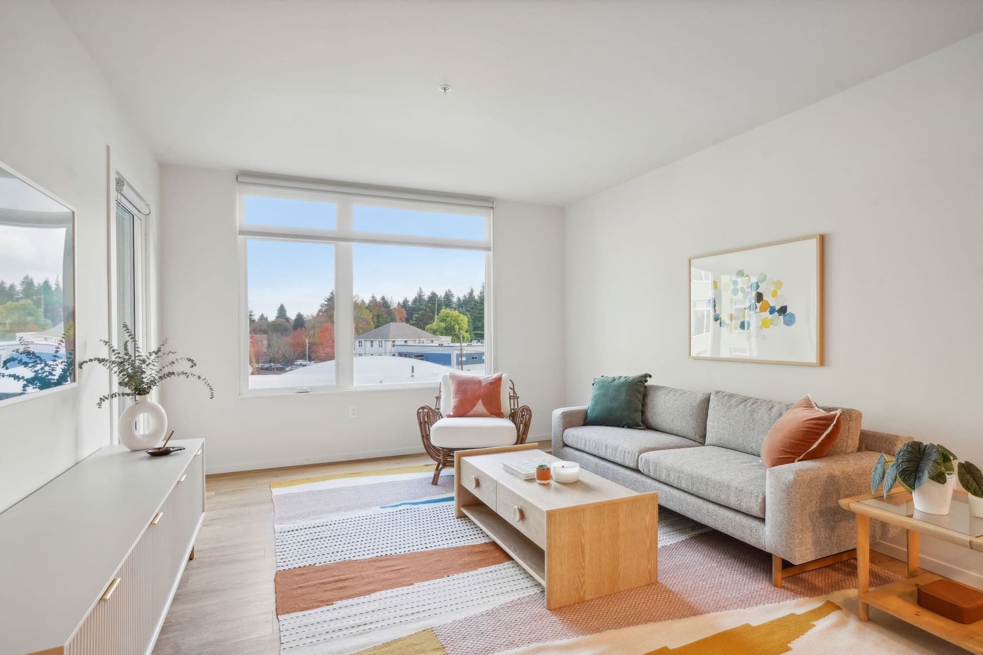 Bright modern living room with gray sofa, wooden coffee table, colorful rug, and large window view