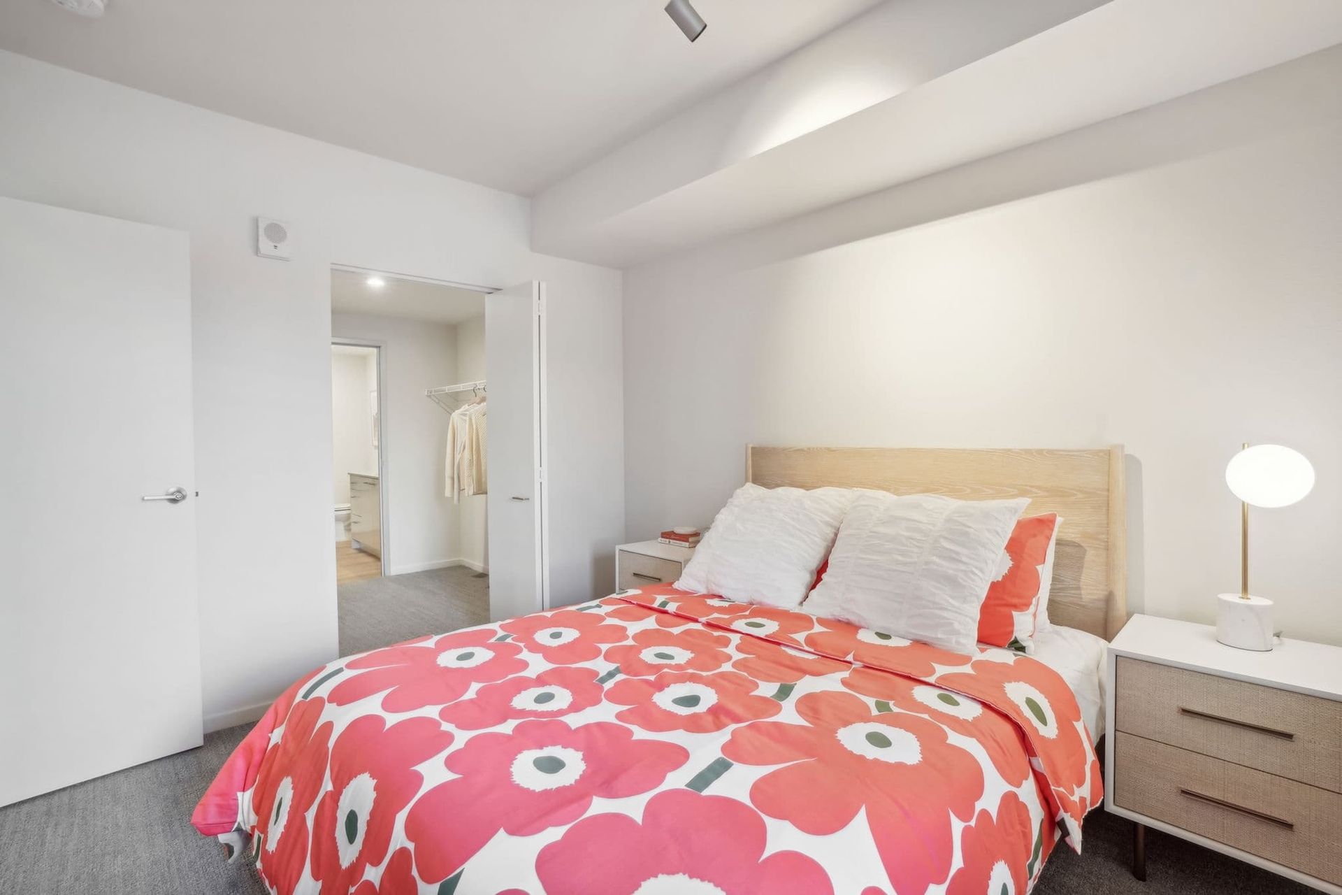 Bright bedroom with a red floral bedspread, white walls, and a bedside lamp