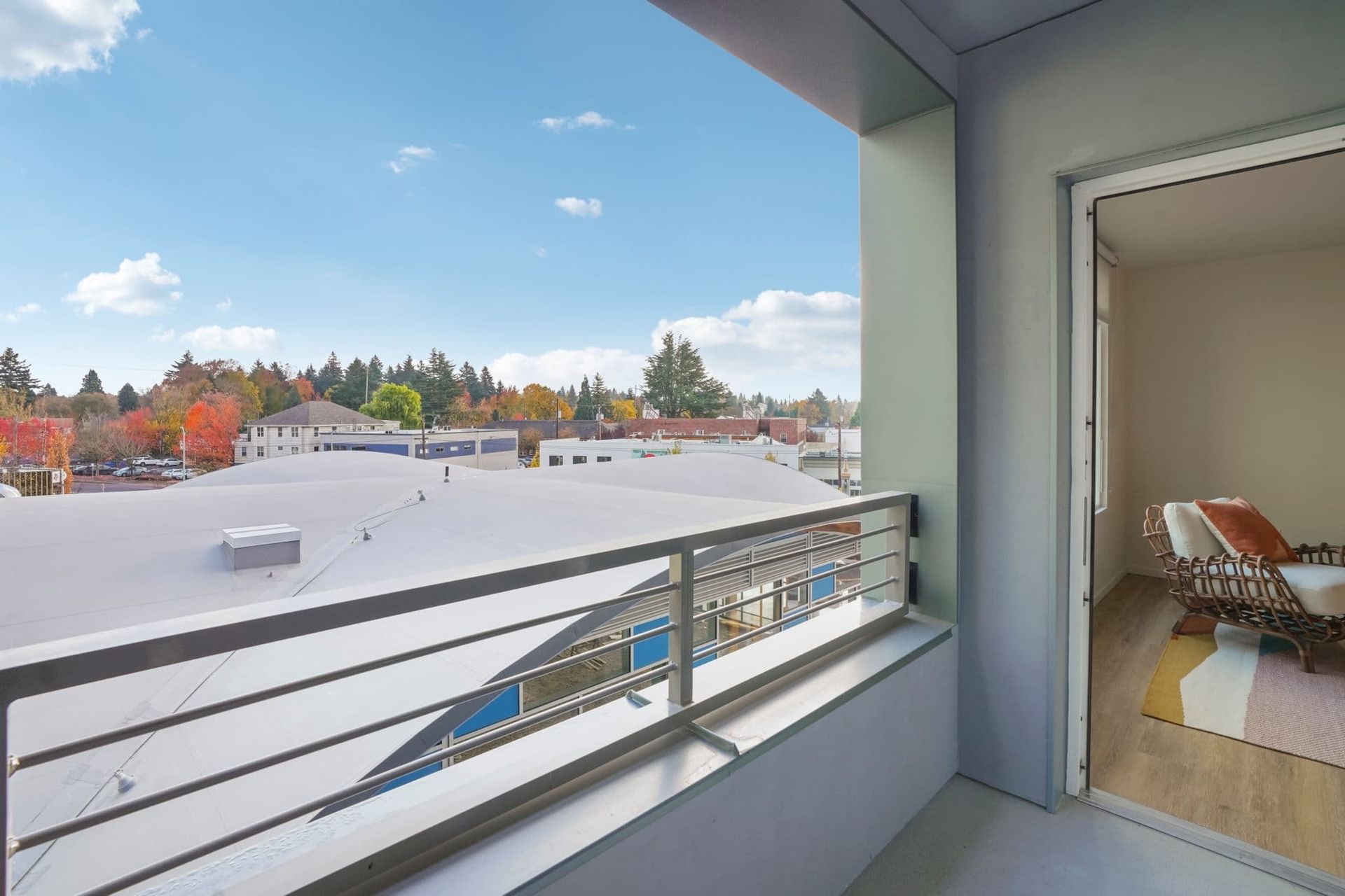 Balcony overlooking a snow-covered rooftop and autumn trees, with a doorway to a furnished room