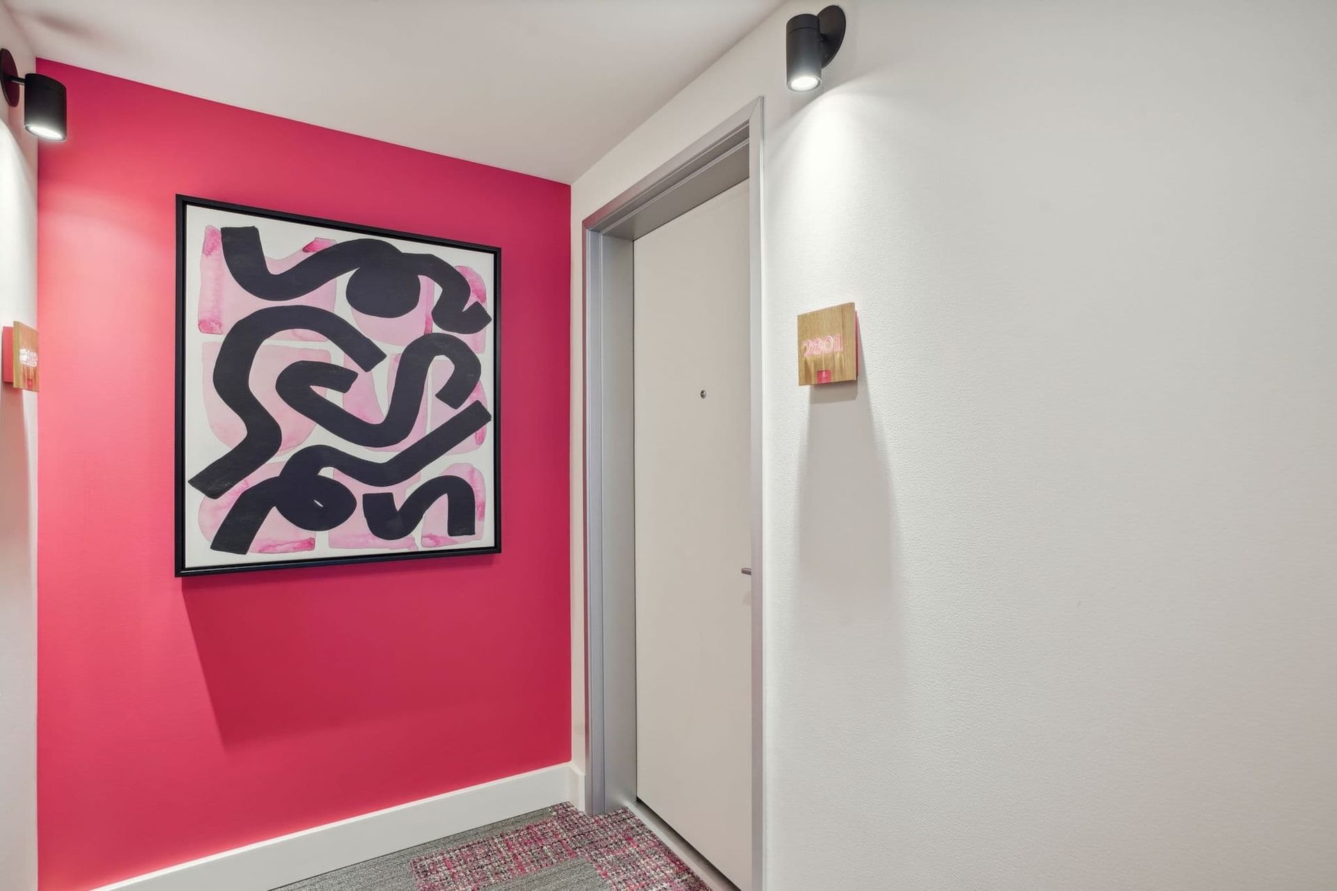 Hallway with a bright pink accent wall, abstract black-and-white artwork, and a white door.