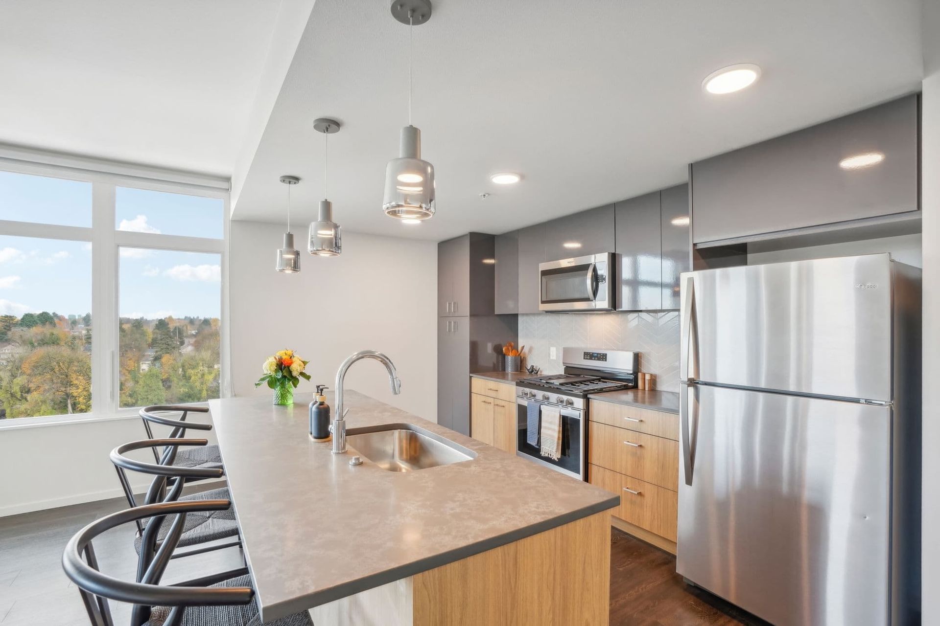 Modern kitchen with stainless steel appliances, island seating, and large windows overlooking trees