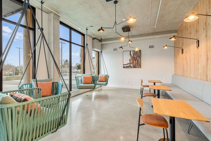 Modern café interior with large windows, hanging chairs, and wooden tables along a long bench.