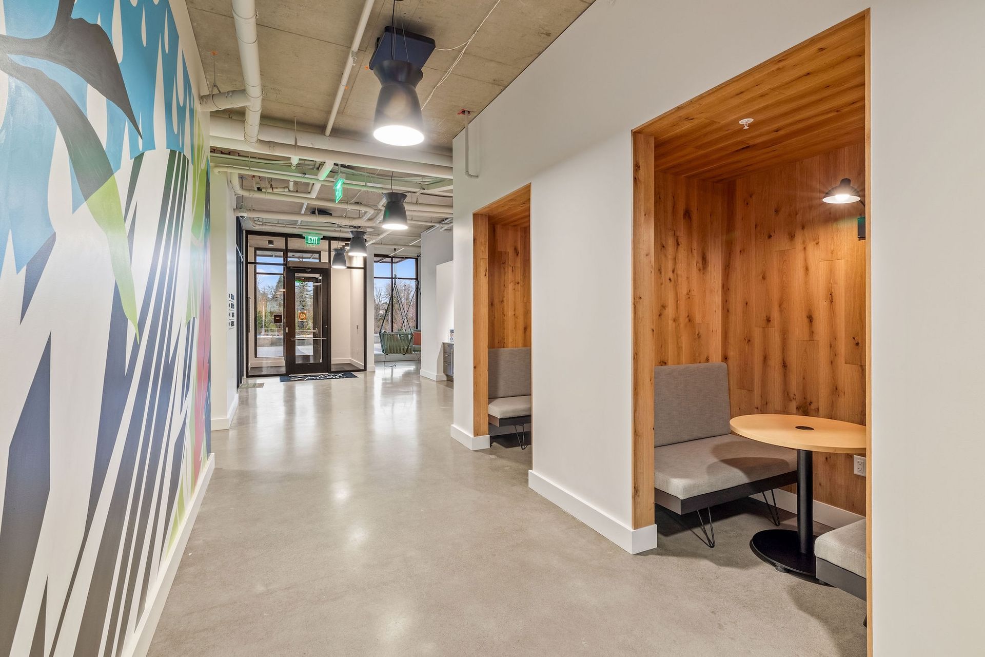 Modern office hallway with wood-paneled alcoves, desks, and colorful mural wall