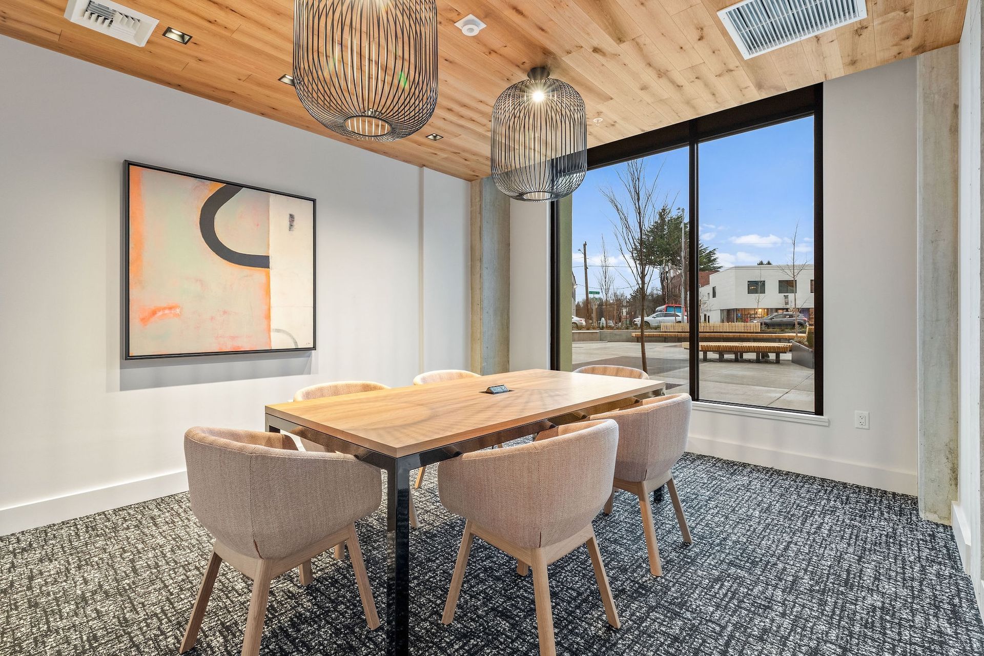 Modern meeting room with wood ceiling, pendant lights, table, upholstered chairs, and large windows.