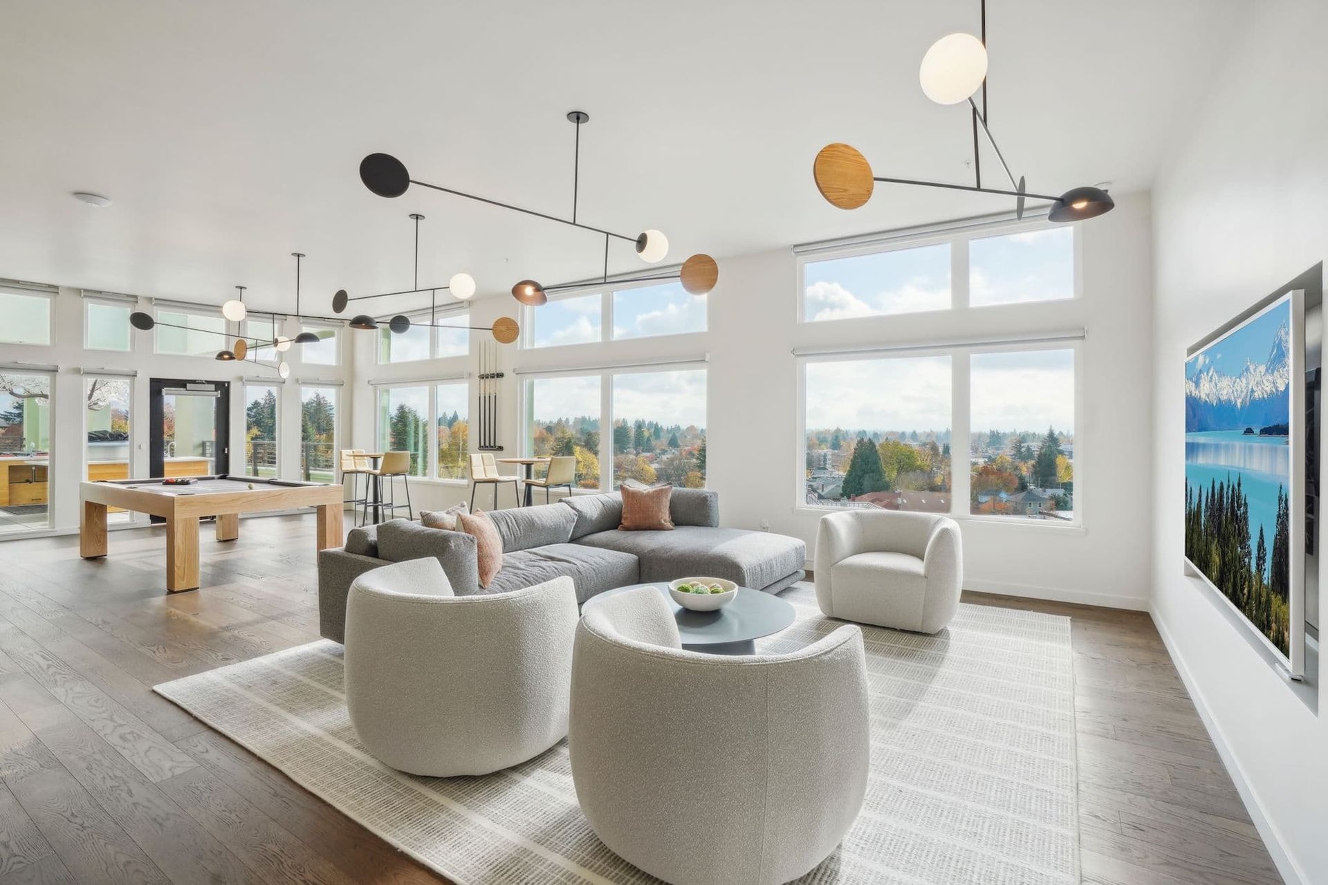 Modern living room with large windows, white chairs, gray sofas, and hanging globe lights