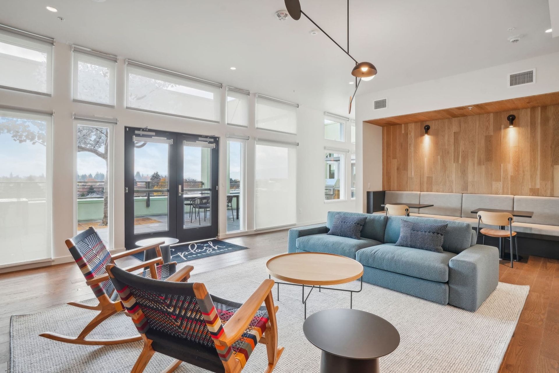 Bright modern living room with blue sofa, lounge chairs, large windows, and wood-paneled wall