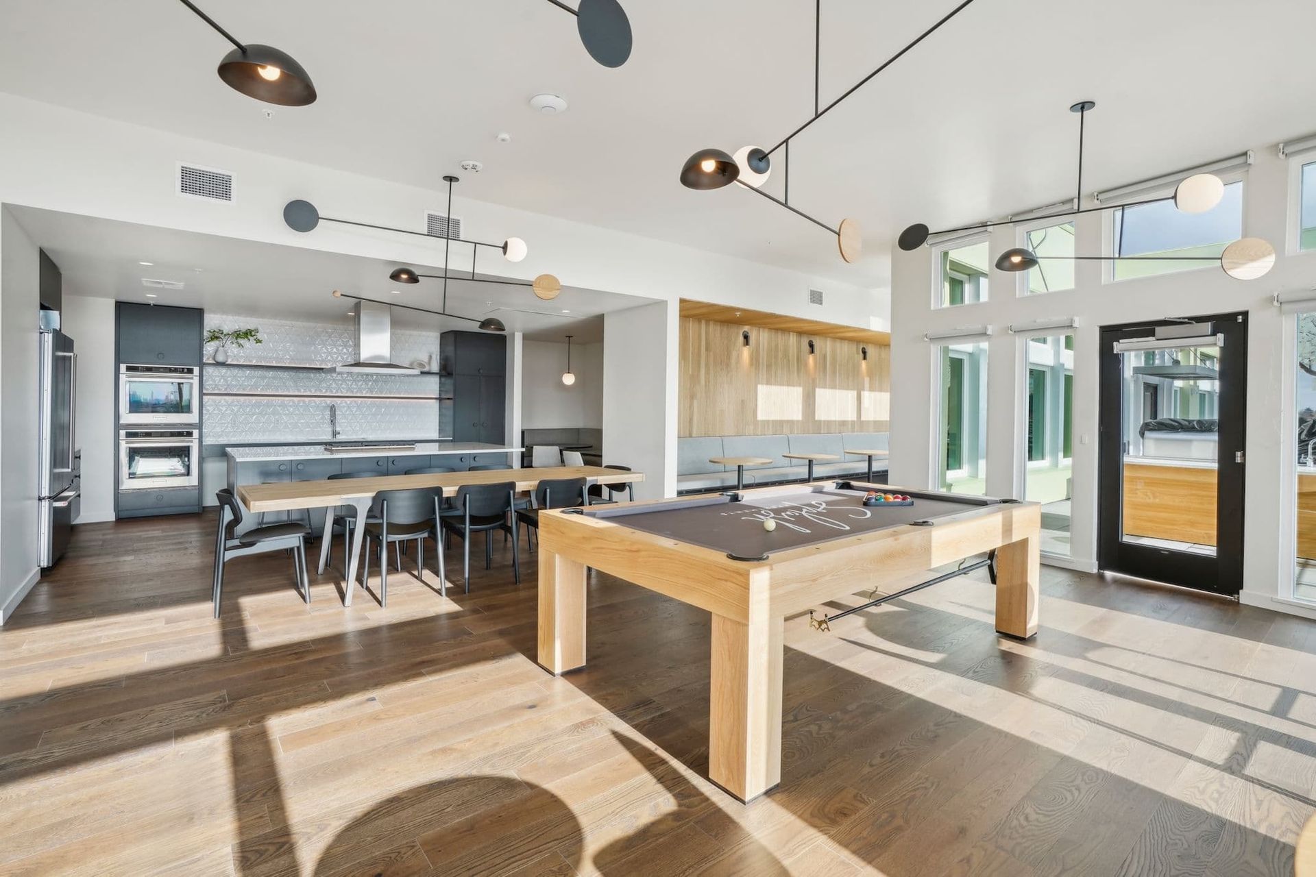 Bright modern kitchen and game room with pool table, bar stools, and large windows
