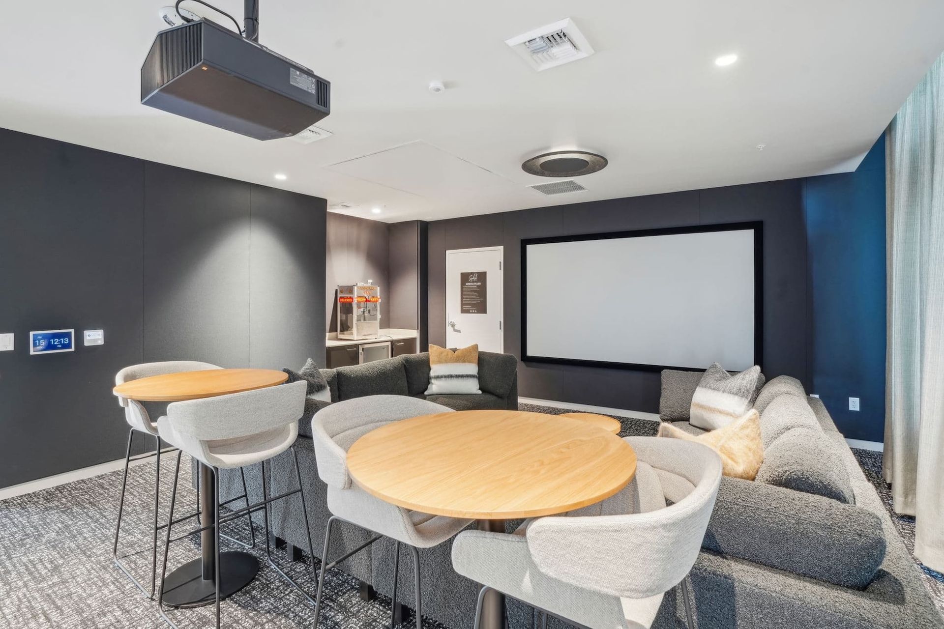 Modern lounge with round tables, gray chairs, a projector screen, and blue accent wall